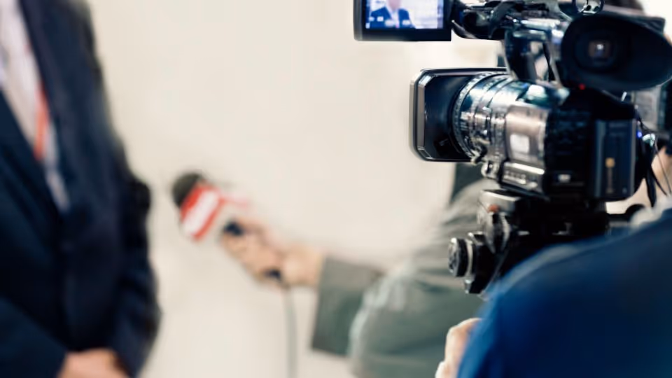 Row of professional video cameras on tripods operated by people in a press or media setting.