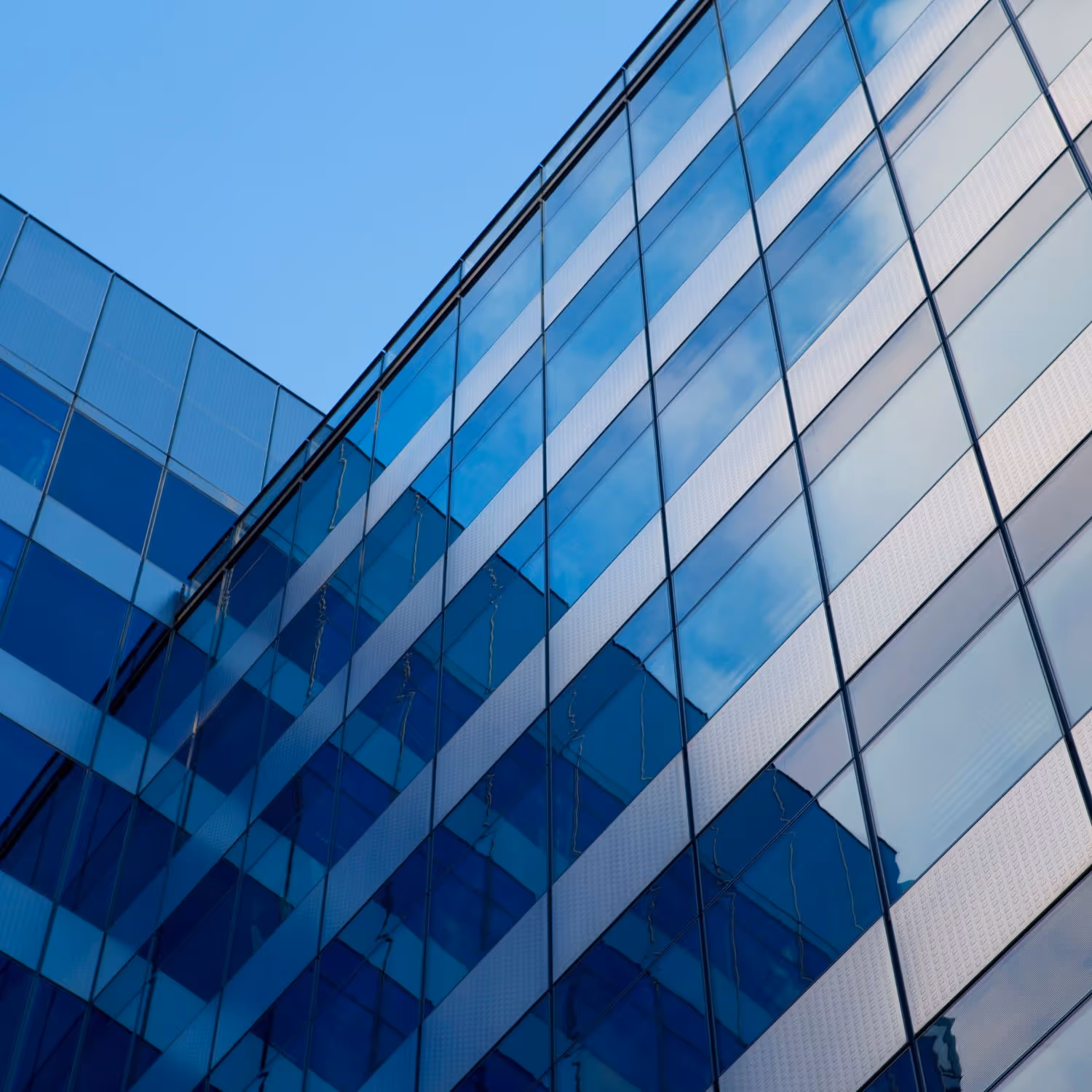 Modern glass building reflecting blue sky and clouds in its mirrored windows.