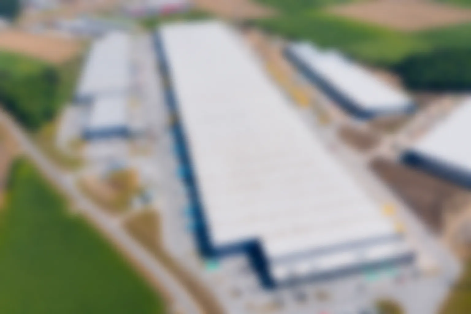Blurred aerial view of a large industrial warehouse complex surrounded by farmland.