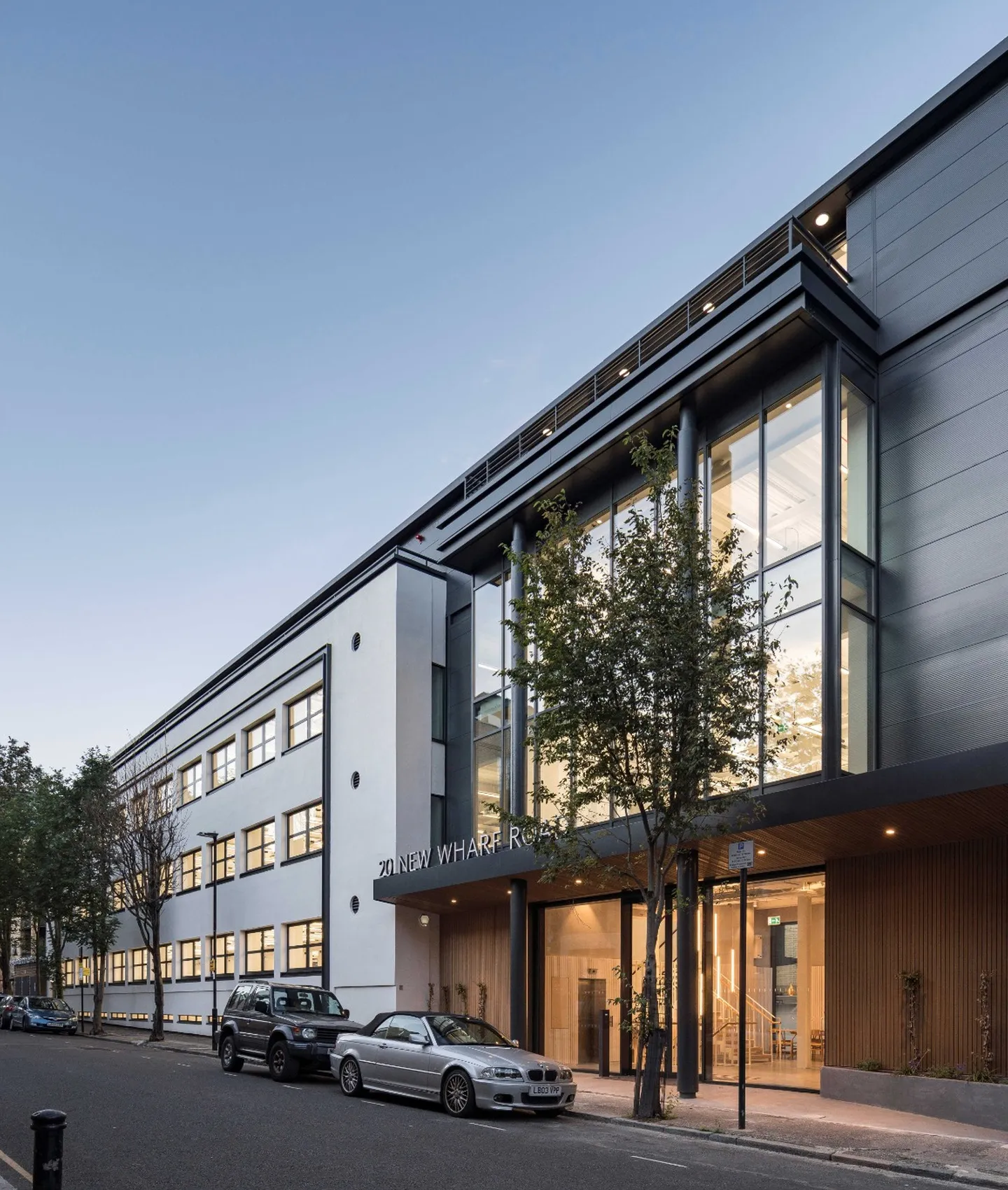 Modern commercial office building with large windows, landscaped entrance, and street parking.