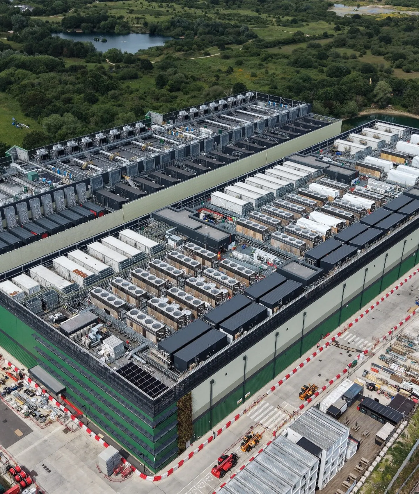 Aerial view of a large data center facility with rooftop cooling equipment surrounded by green countryside.