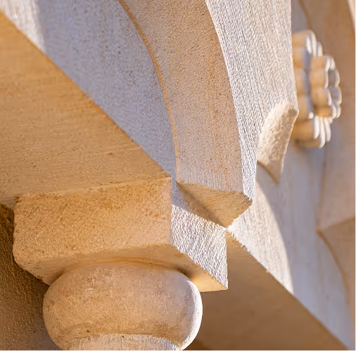 Close-up of a beige stone architectural column and detailed arch with textured surface in sunlight.