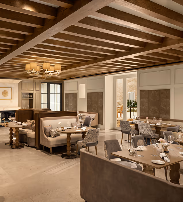 Elegant dining room with wooden ceiling beams, beige booths, and tables set with glassware and plates.