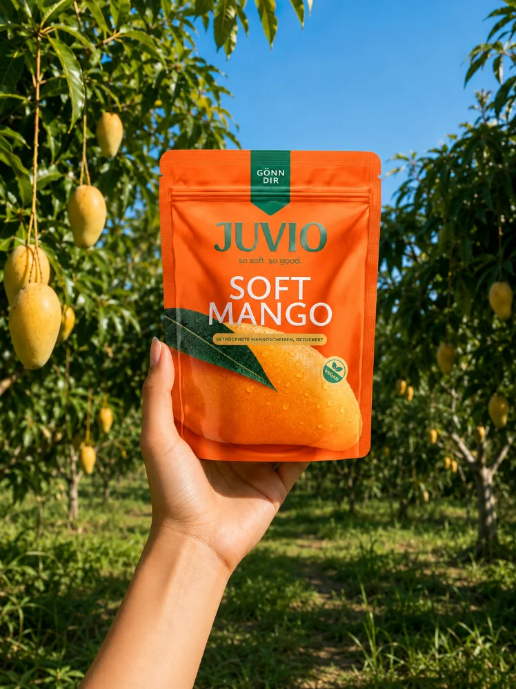 Hand hält eine JUVIO Soft Mango Packung auf einer Mangoplantage