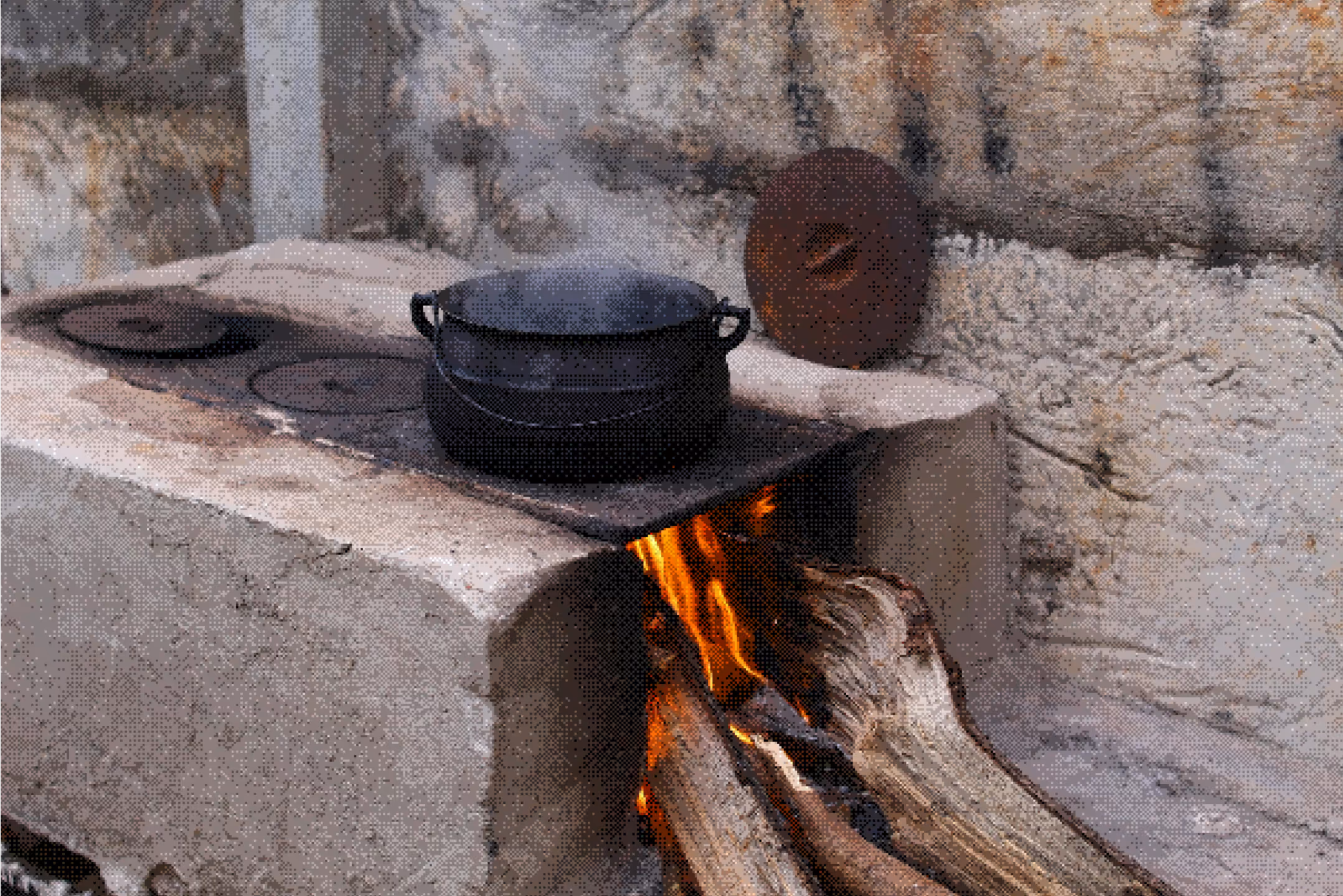Traditional outdoor wood-burning stove with a black pot steaming on top and firewood burning inside.