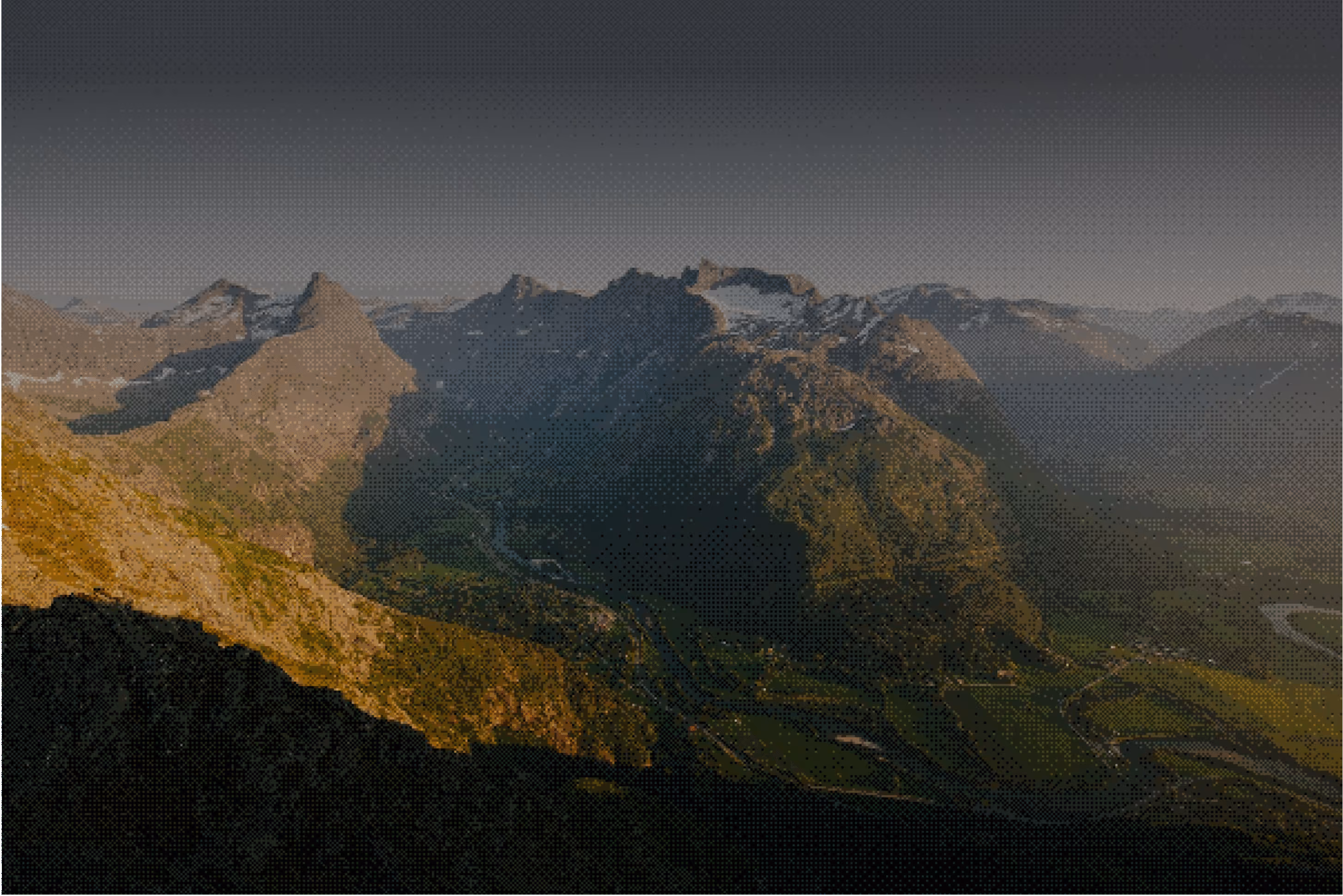 Sunlit mountain peaks with shadowed valleys and green fields below under a clear sky.