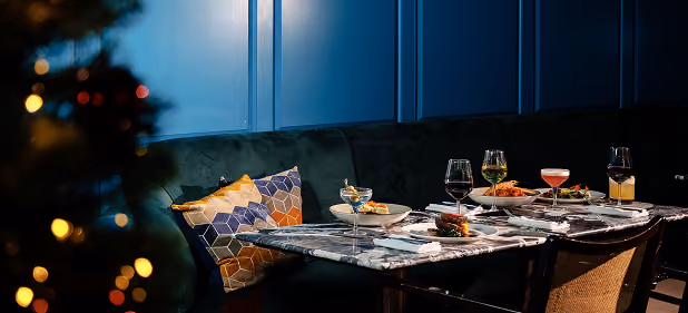 A corner table at The Grayson set with wine and cocktails beside the Christmas tree