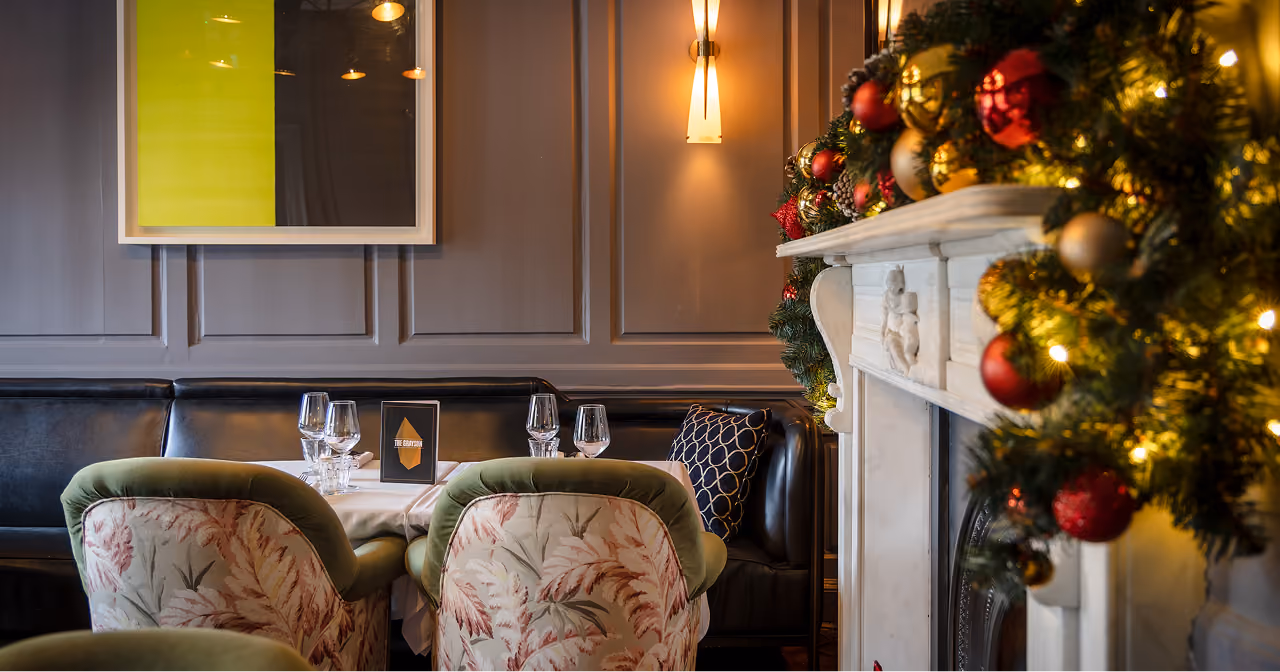 Armchairs at a set table beside the garlanded marble fireplace at The Grayson