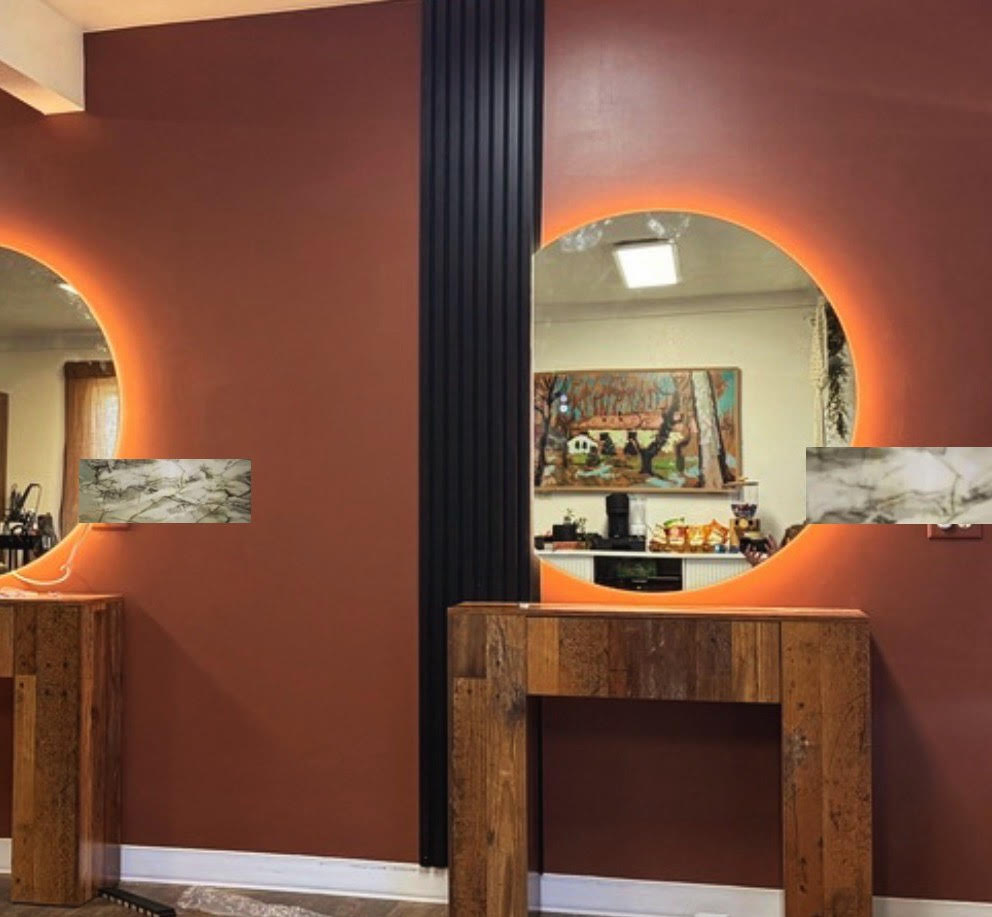 Rust-colored wall with two round backlit mirrors above rustic wooden consoles in a modern interior.