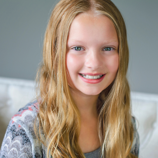Smiling young girl with long blonde hair and blue eyes wearing a gray patterned sweater.