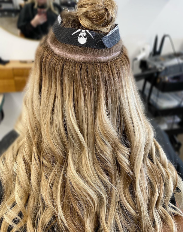 Woman with long, wavy blonde hair styled with soft curls viewed from the side.