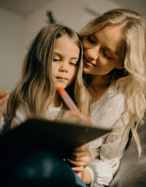 Mother and daughter closely looking at a notepad while the daughter writes with a pen.