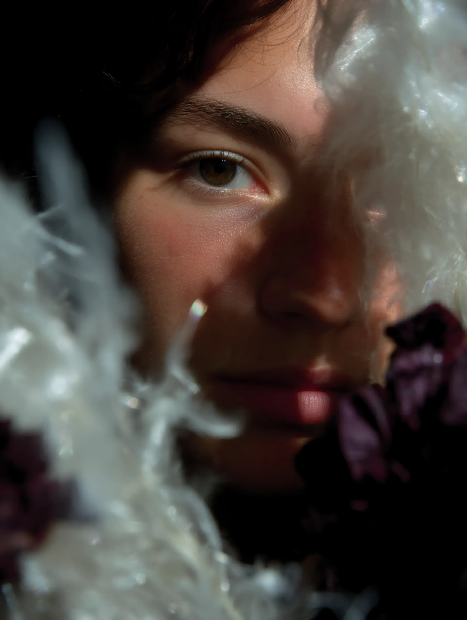 Photo of a woman's face half hidden behind white feathers