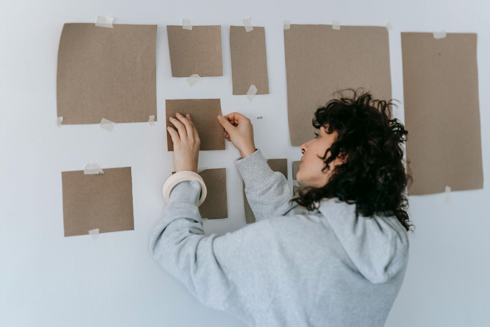 Someone taping paper templates to a wall to test a gallery wall layout before hanging it