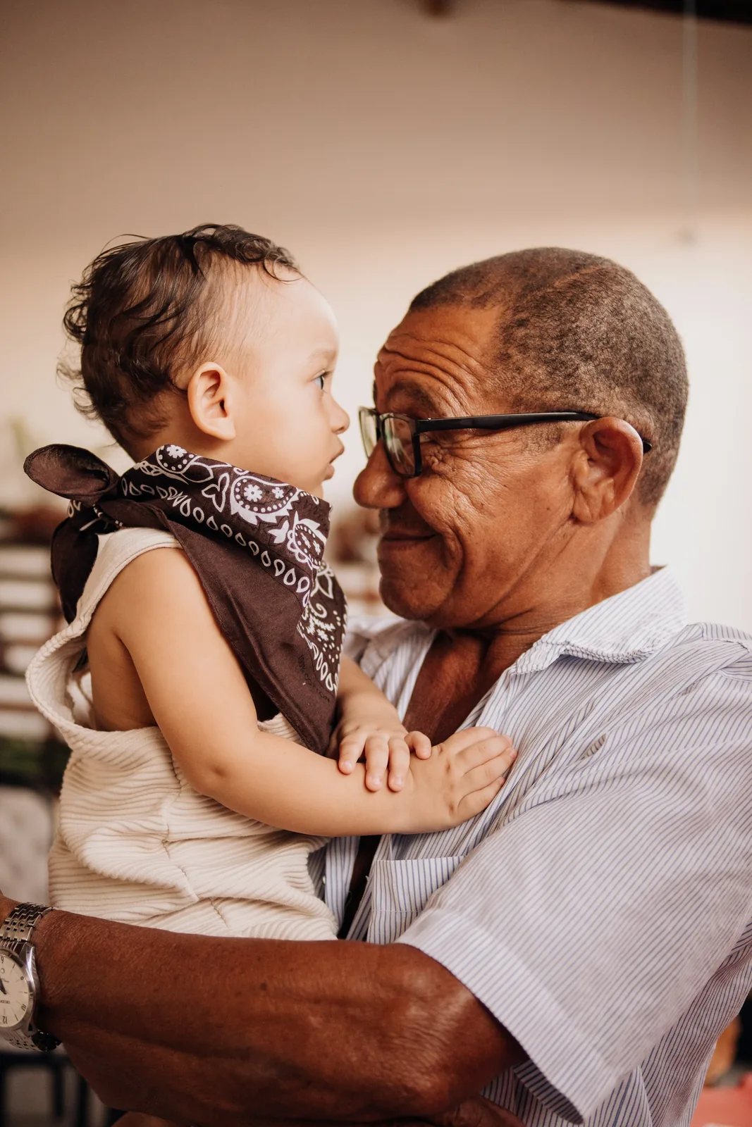 A man crouching outdoors gently holding a smiling toddler who is touching his nose.