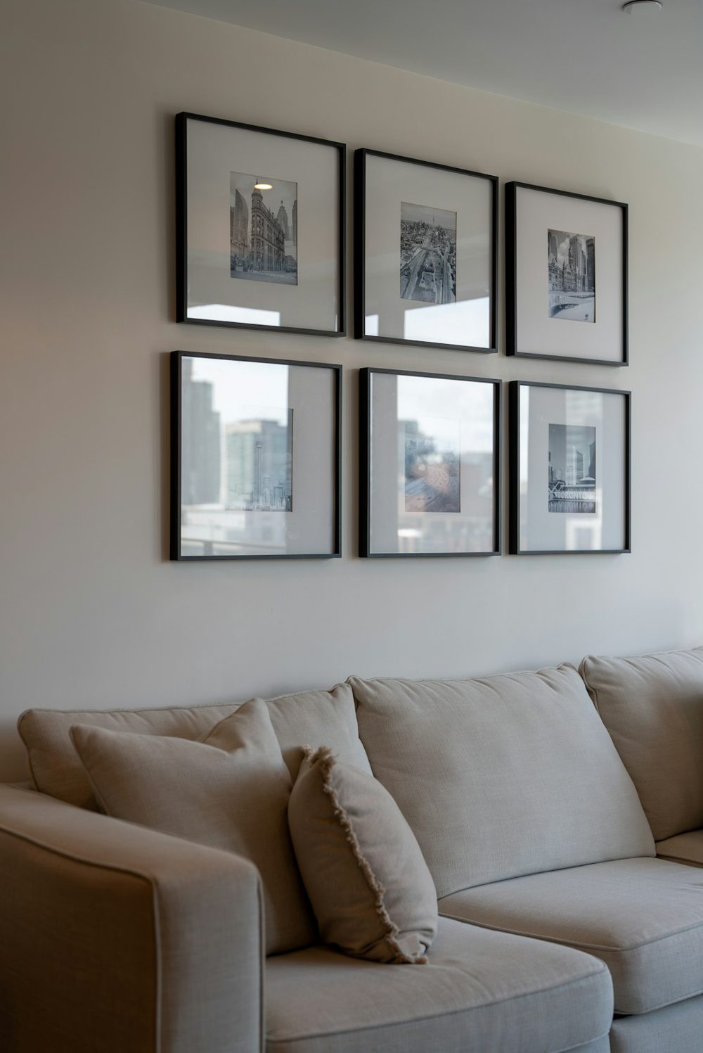Six framed artworks hang above a light-colored sofa