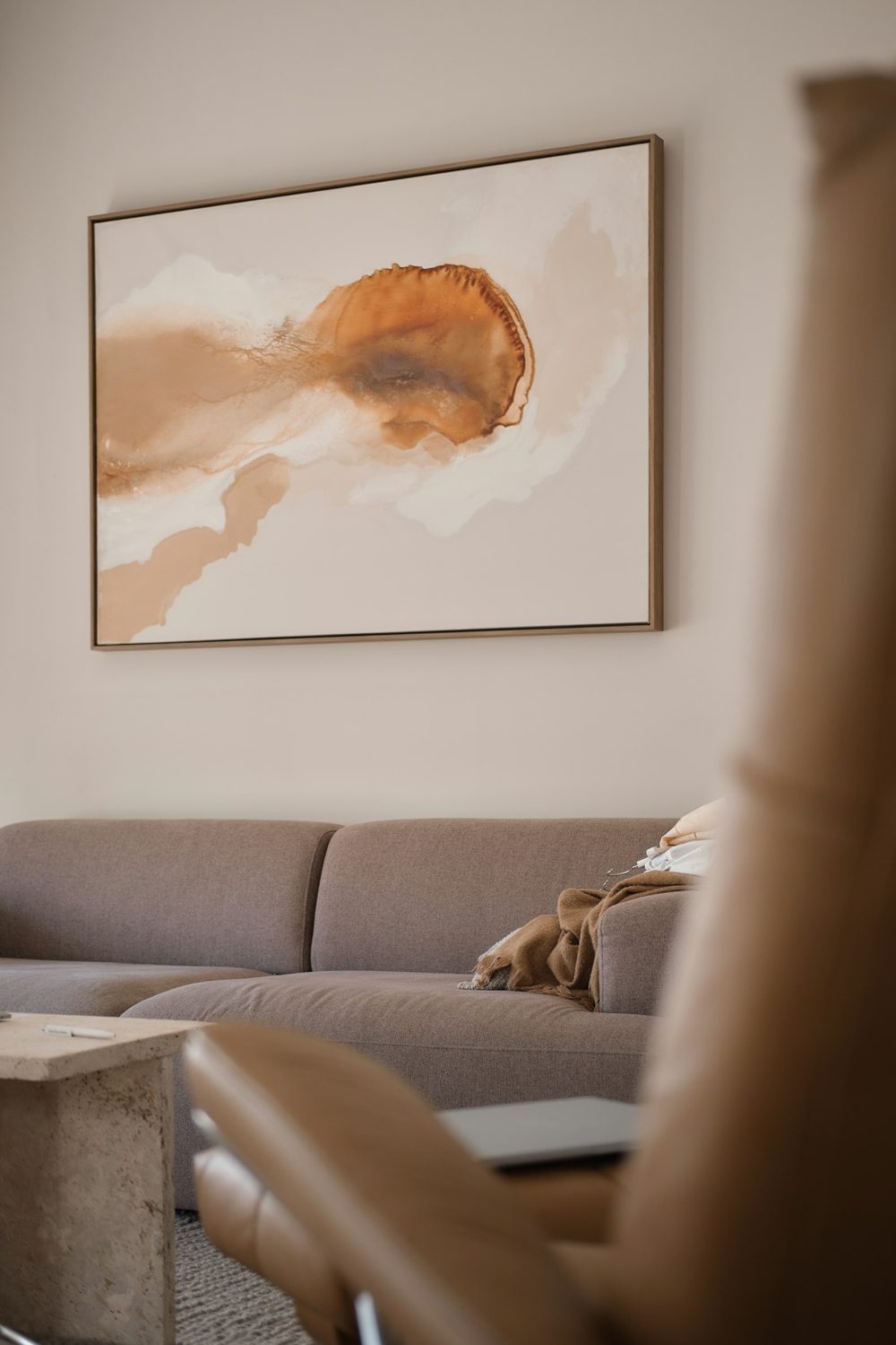A brown sofa with a throw blanket below an abstract painting in a living room