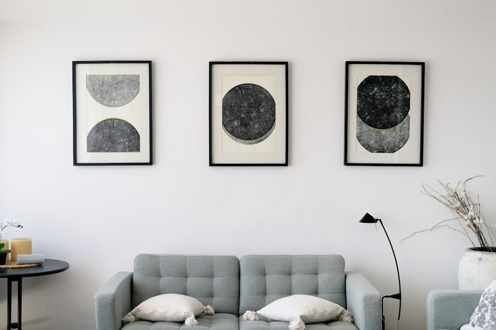 Three abstract art pieces hang above a gray sofa
