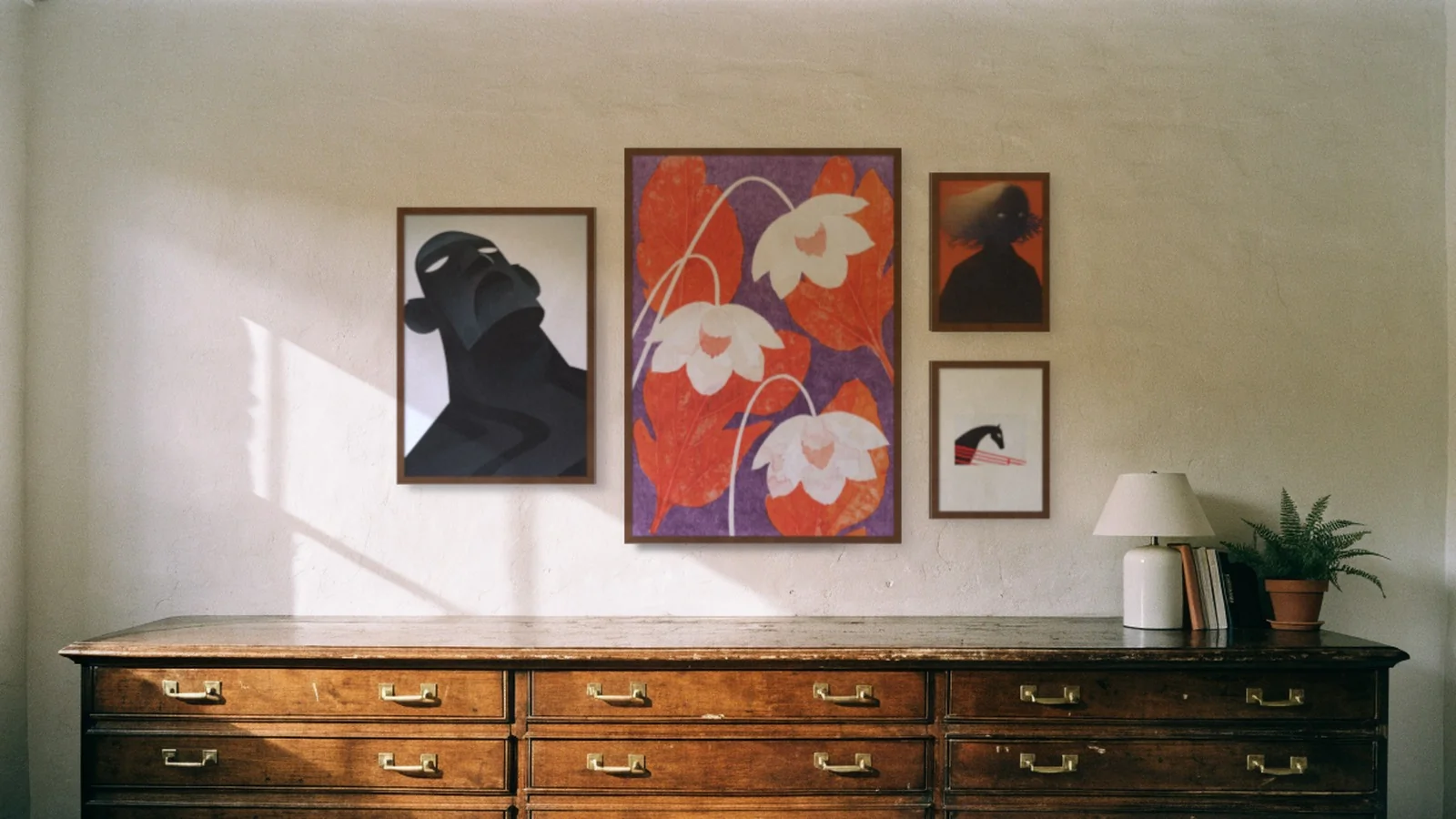 Four prints in walnut frames, grouped around a large floral one, above a wooden chest of drawers