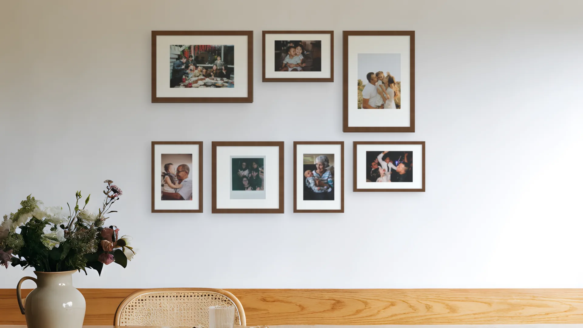 Seven family photos in walnut frames in a classic gallery arrangement above a bench in a dining room