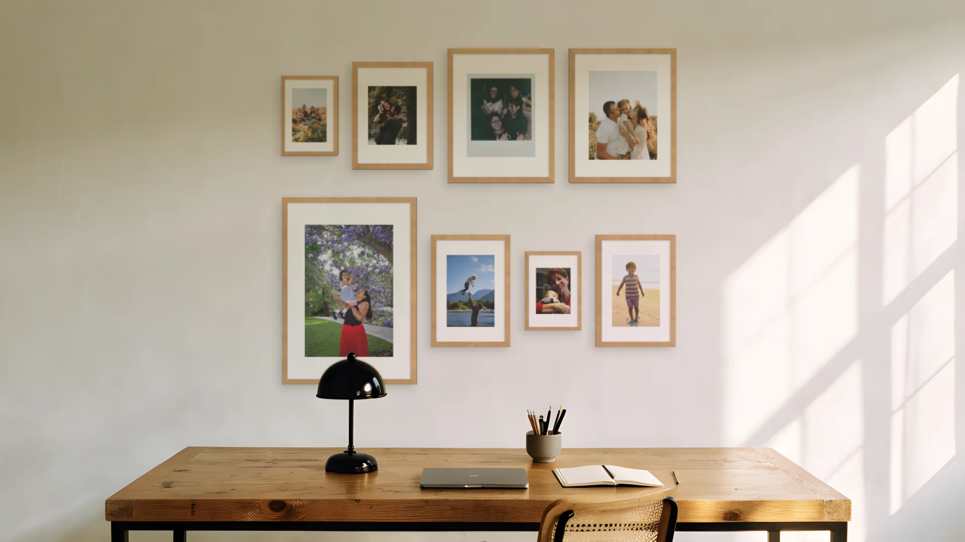 Eight family photos in oak frames in mixed frame sizes above a desk in a home office