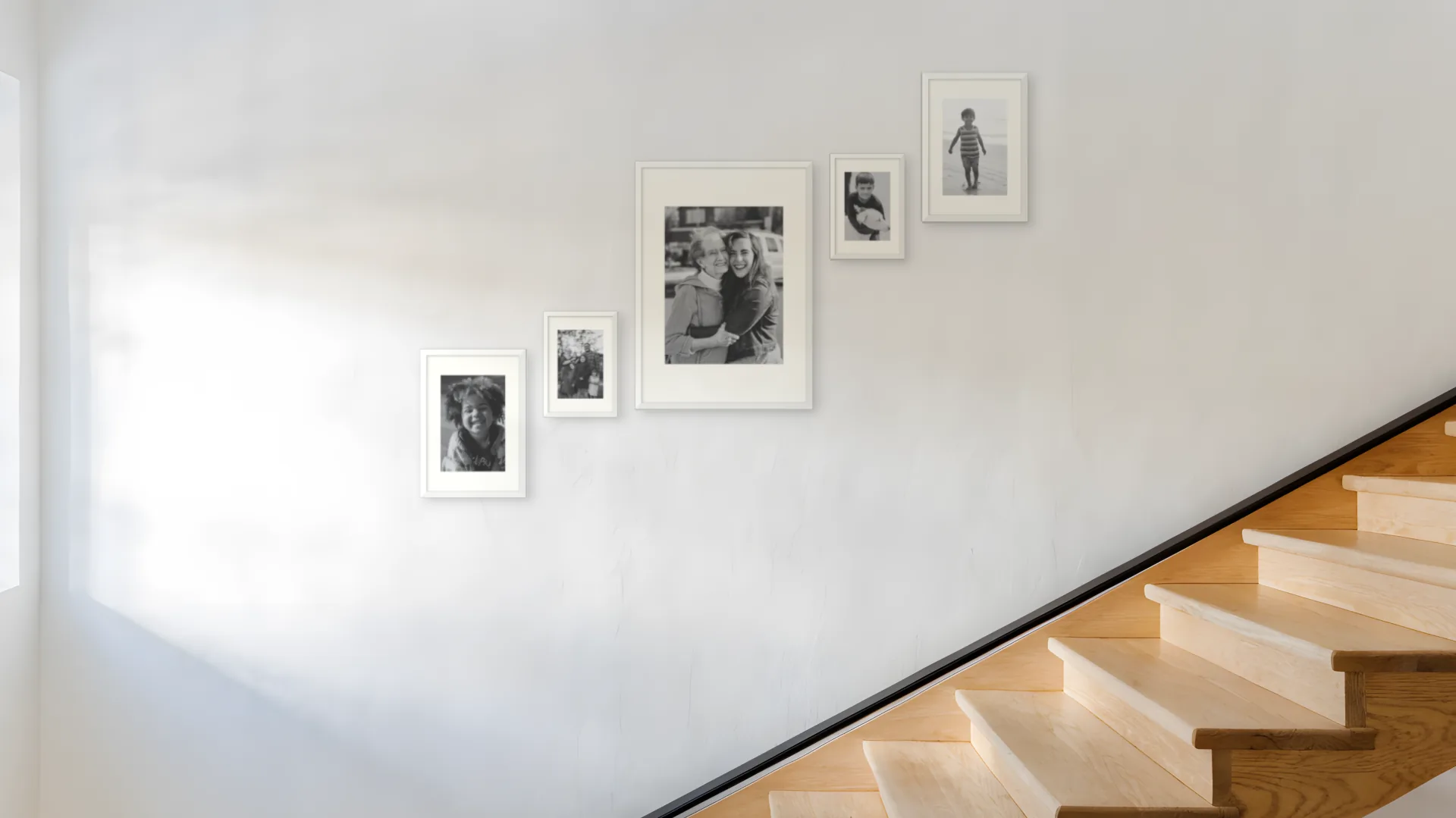 The same staircase wall with five black and white family photos in white frames, planned in Curate