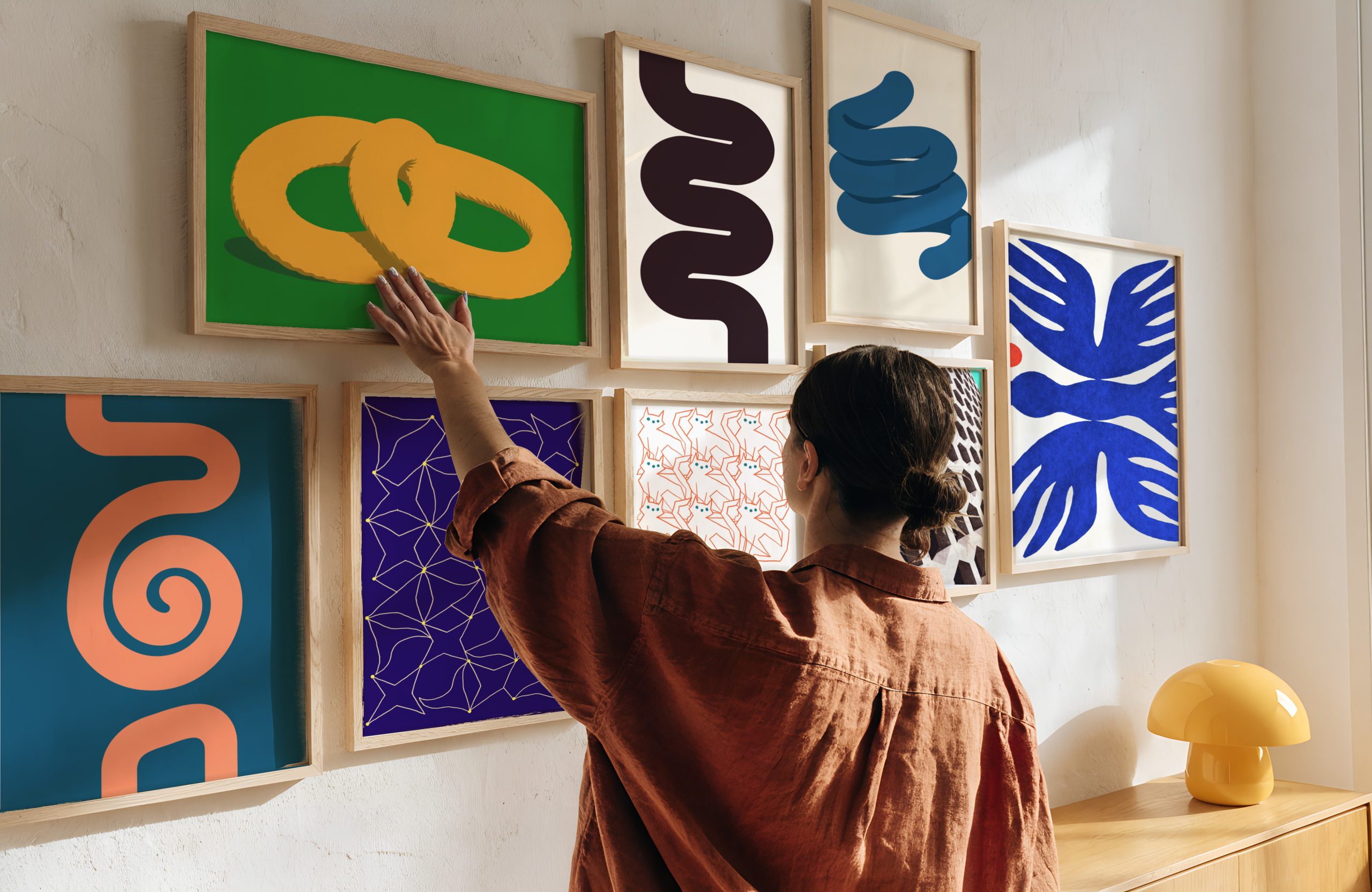 Woman straightening a framed print on a gallery wall of abstract prints