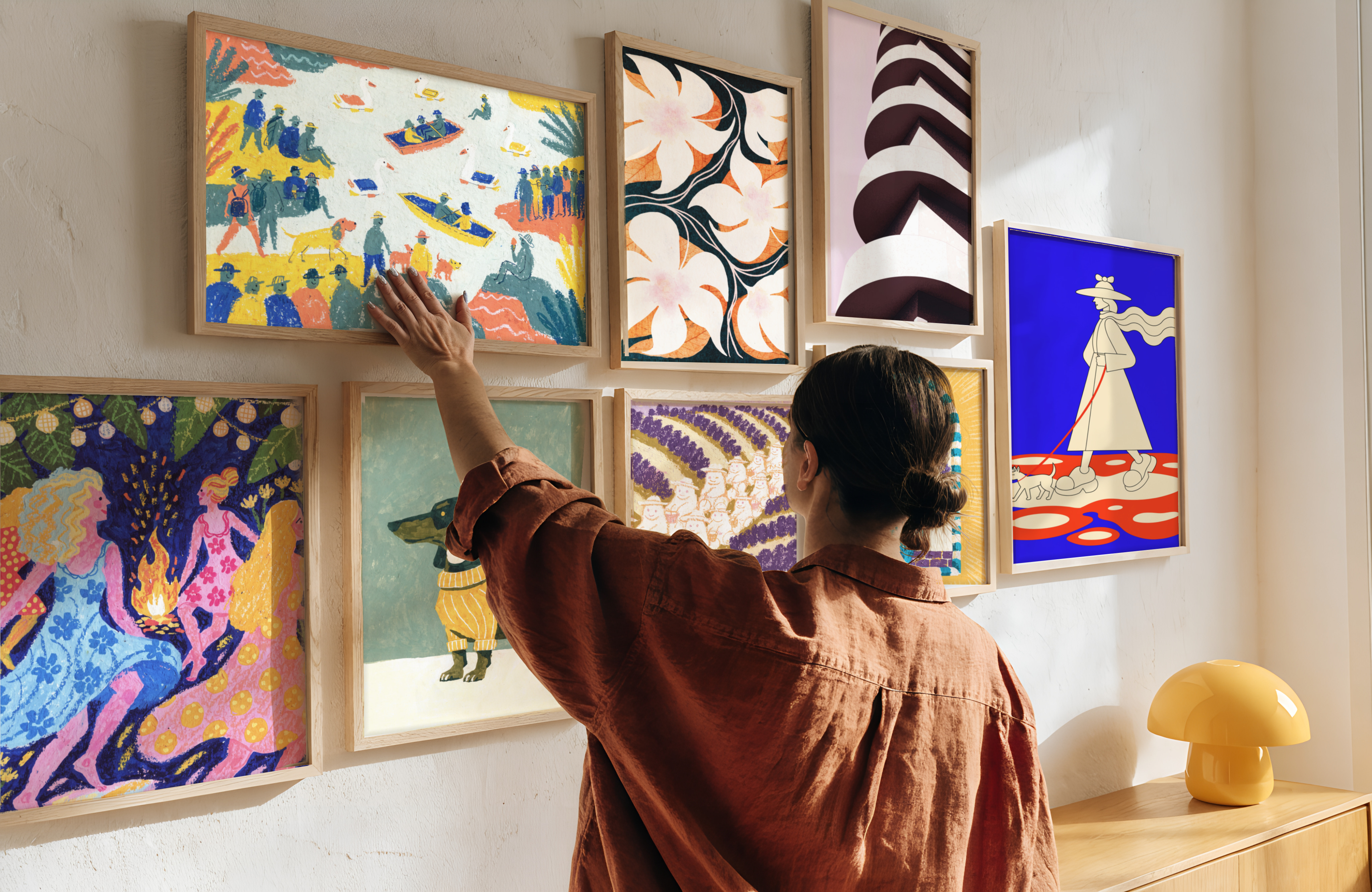 Woman hanging a framed print on a wall of illustrated prints