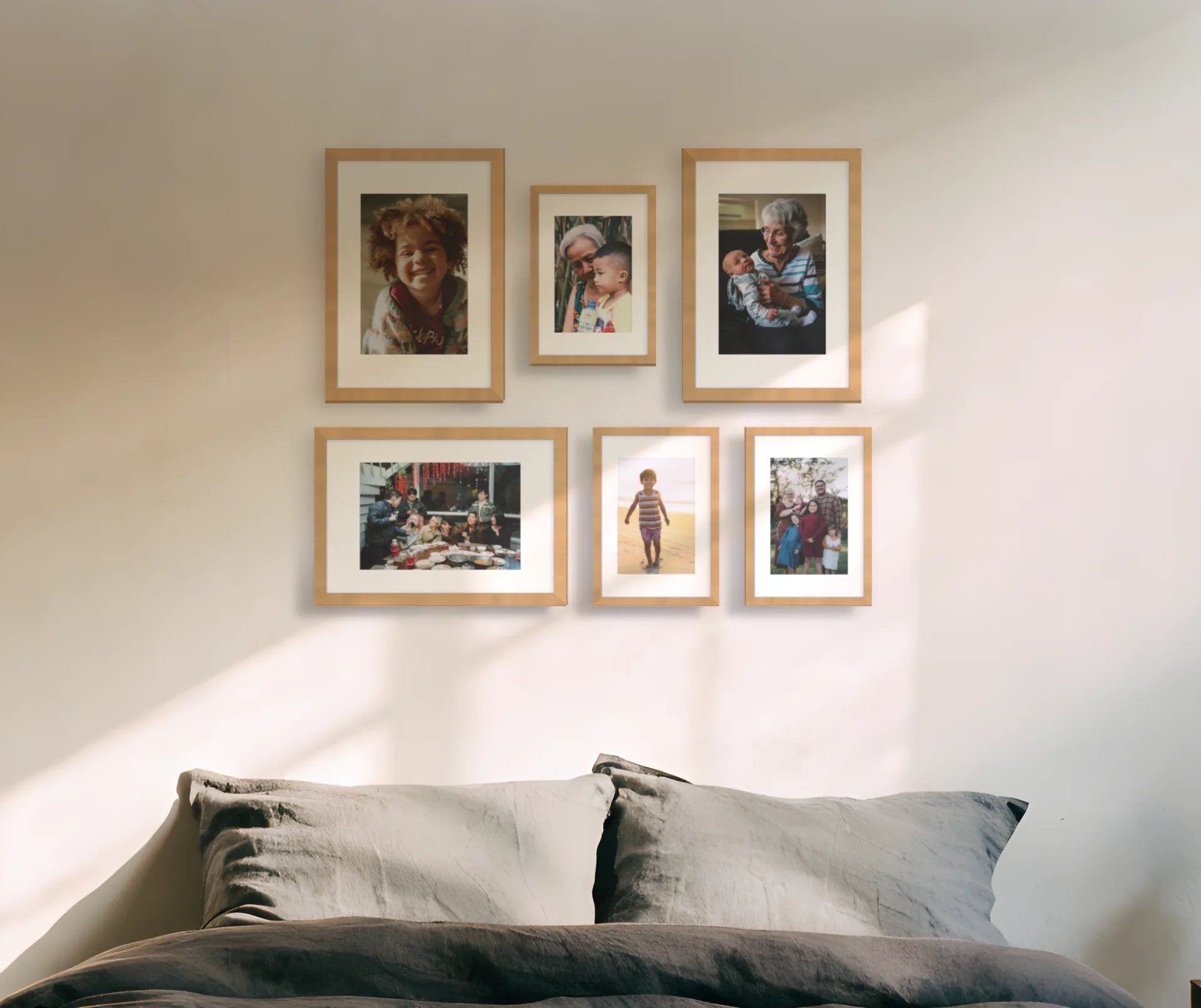 Six family photographs in natural oak frames arranged above a bed on a photo of a bedroom wall