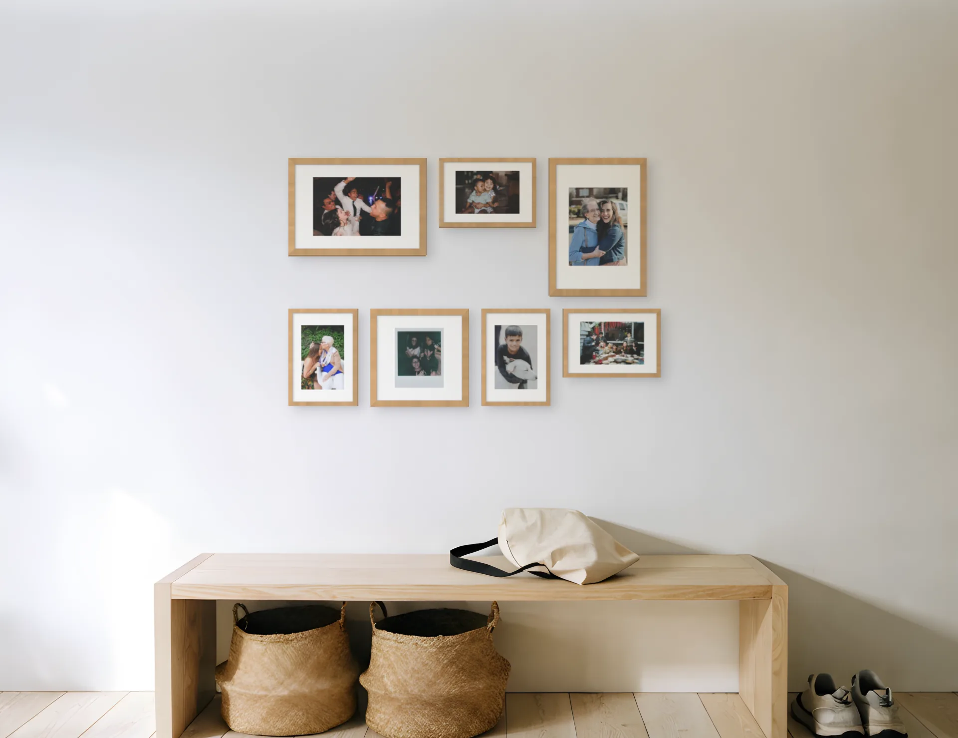 Seven family photos in oak frames in a classic gallery arrangement above a bench in a hallway, planned in Curate