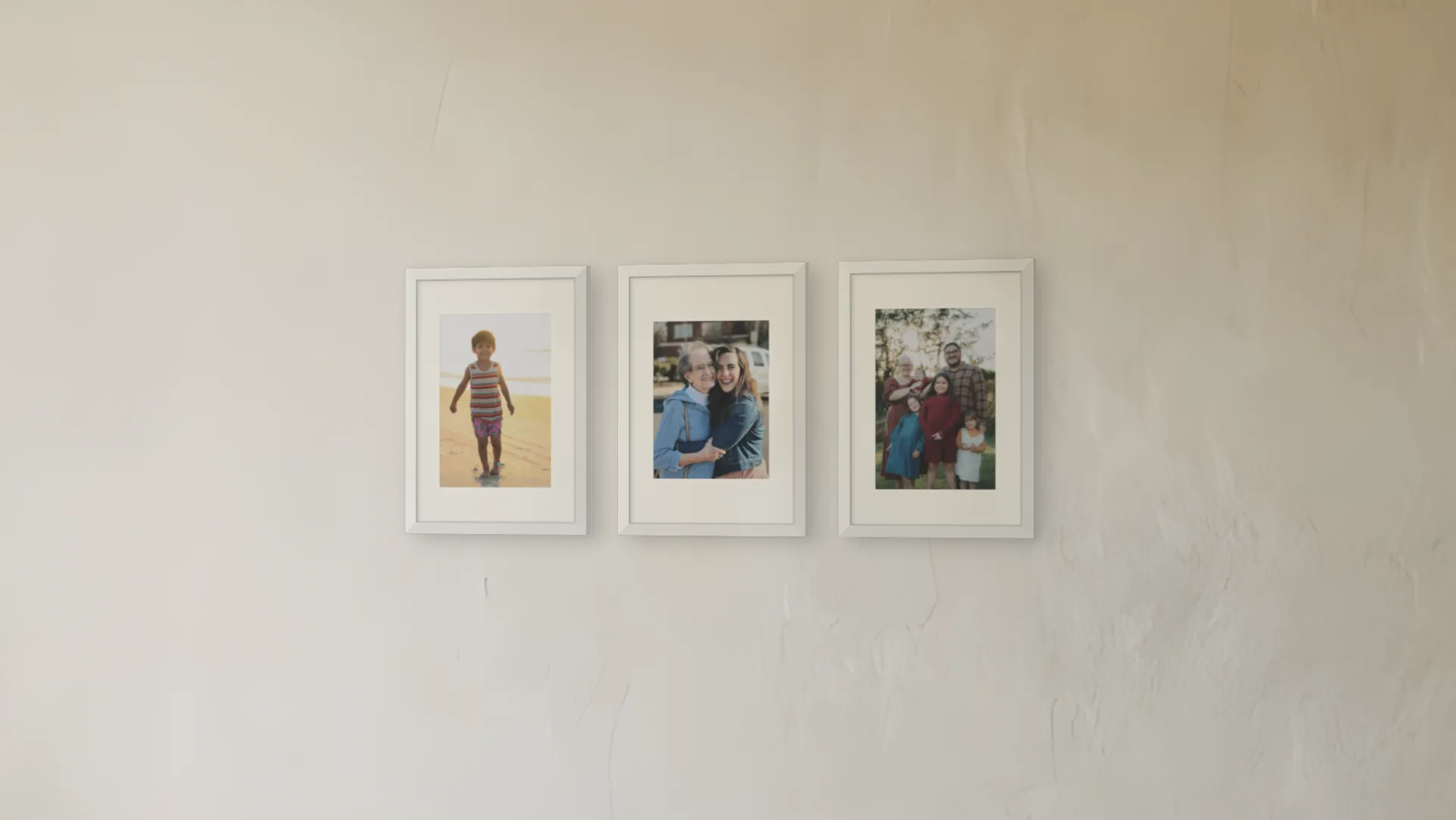 Family photo gallery wall idea: three family photos in white frames in a row on a living room wall.