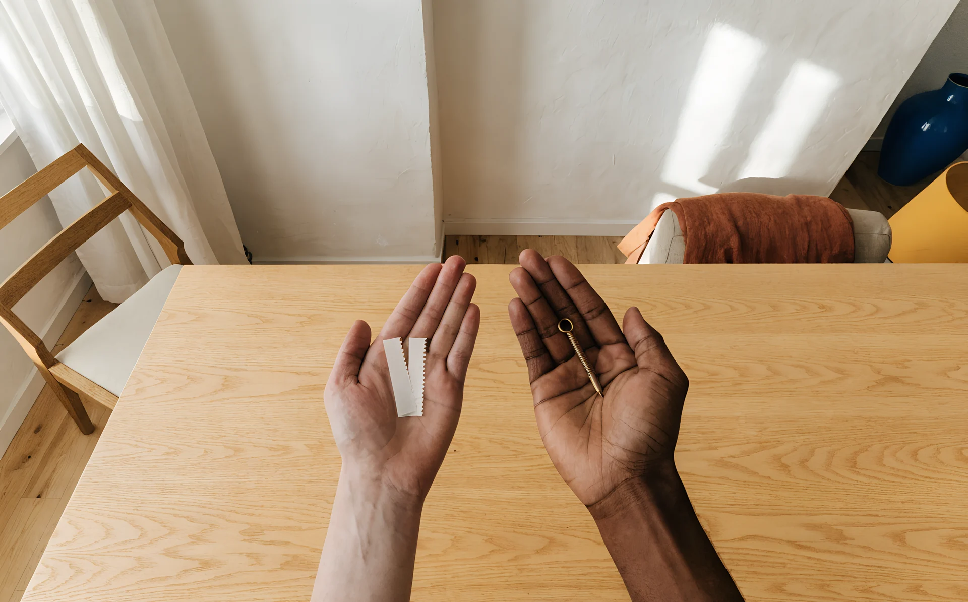 Two hands side by side, one holding adhesive strips and one holding a picture hook and nail