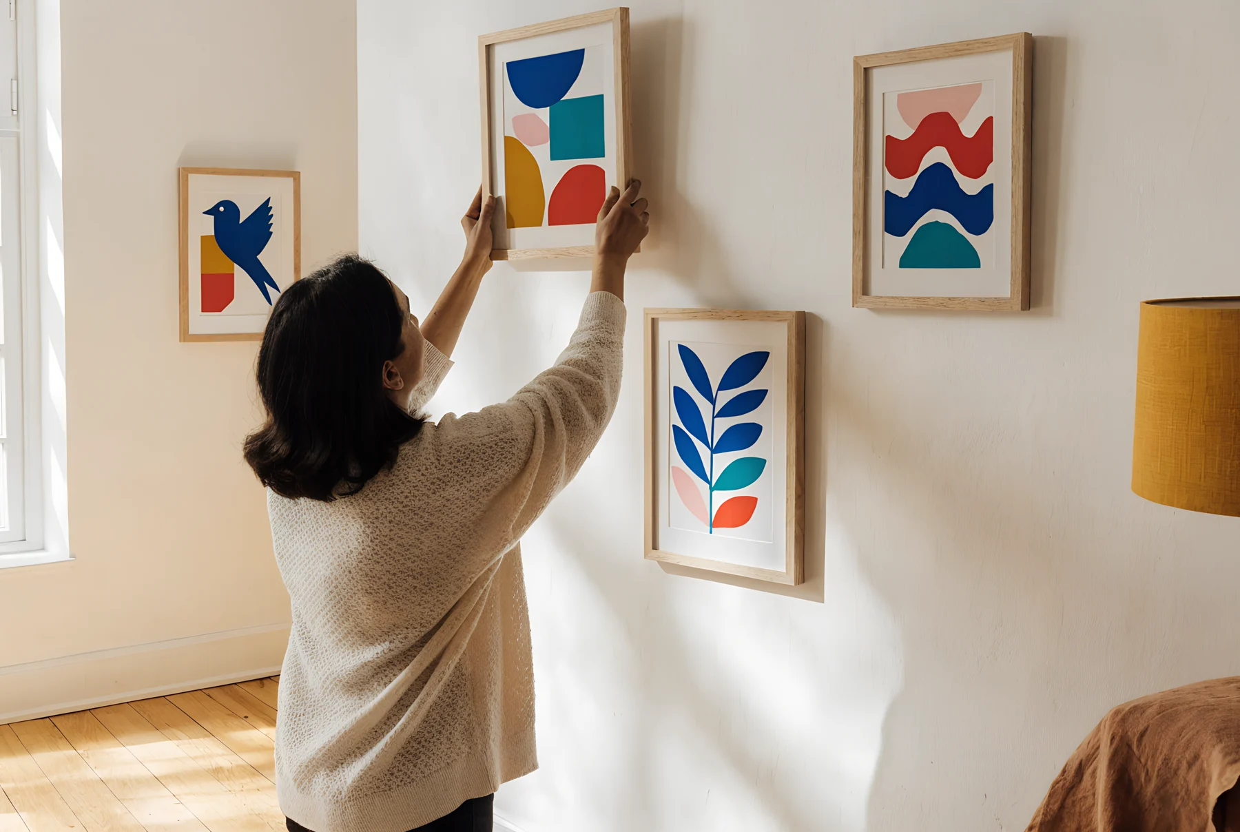 A woman in a cream knit lifts a framed colourful print onto her wall