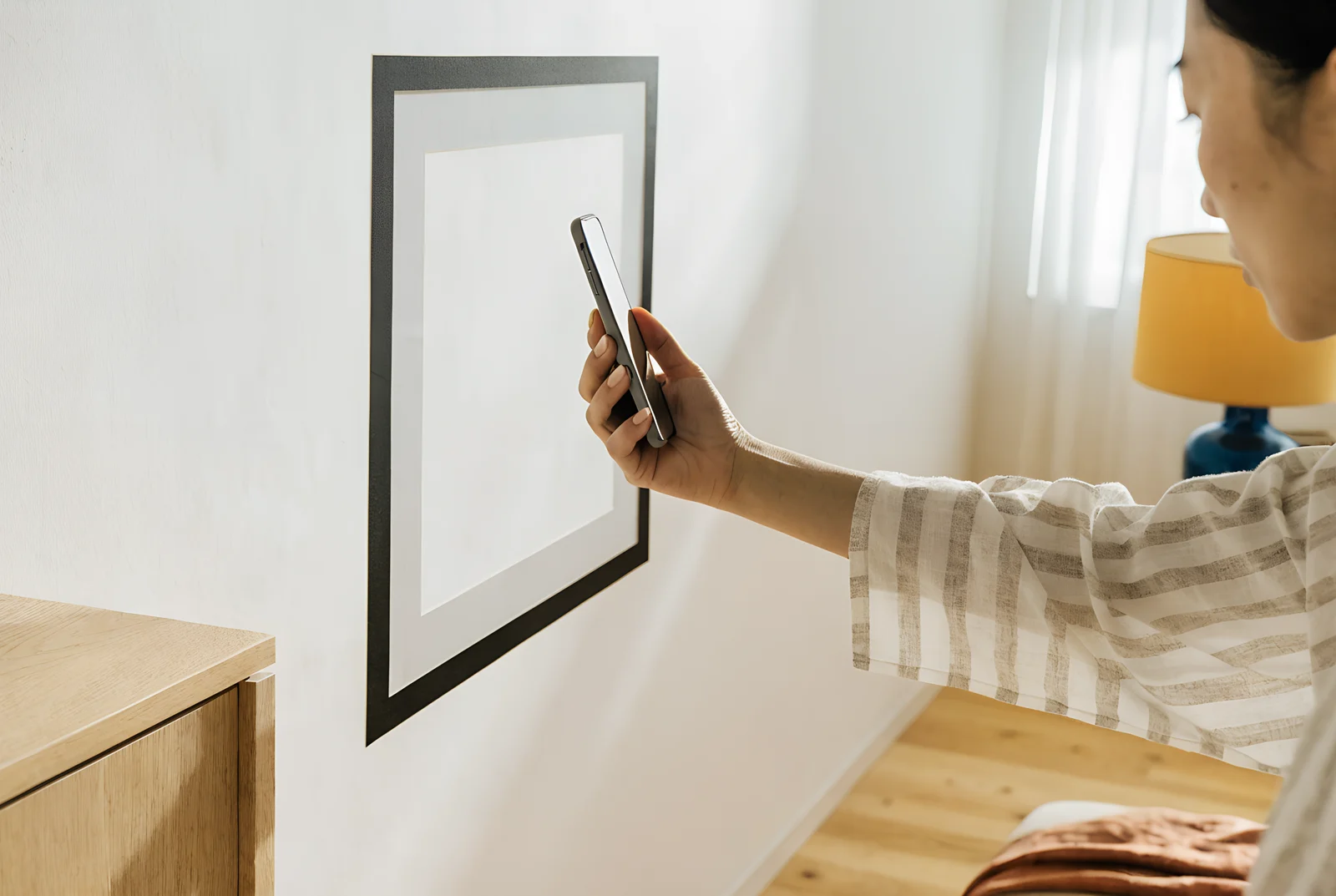 A woman holds up her phone to preview how a large frame will look on her wall