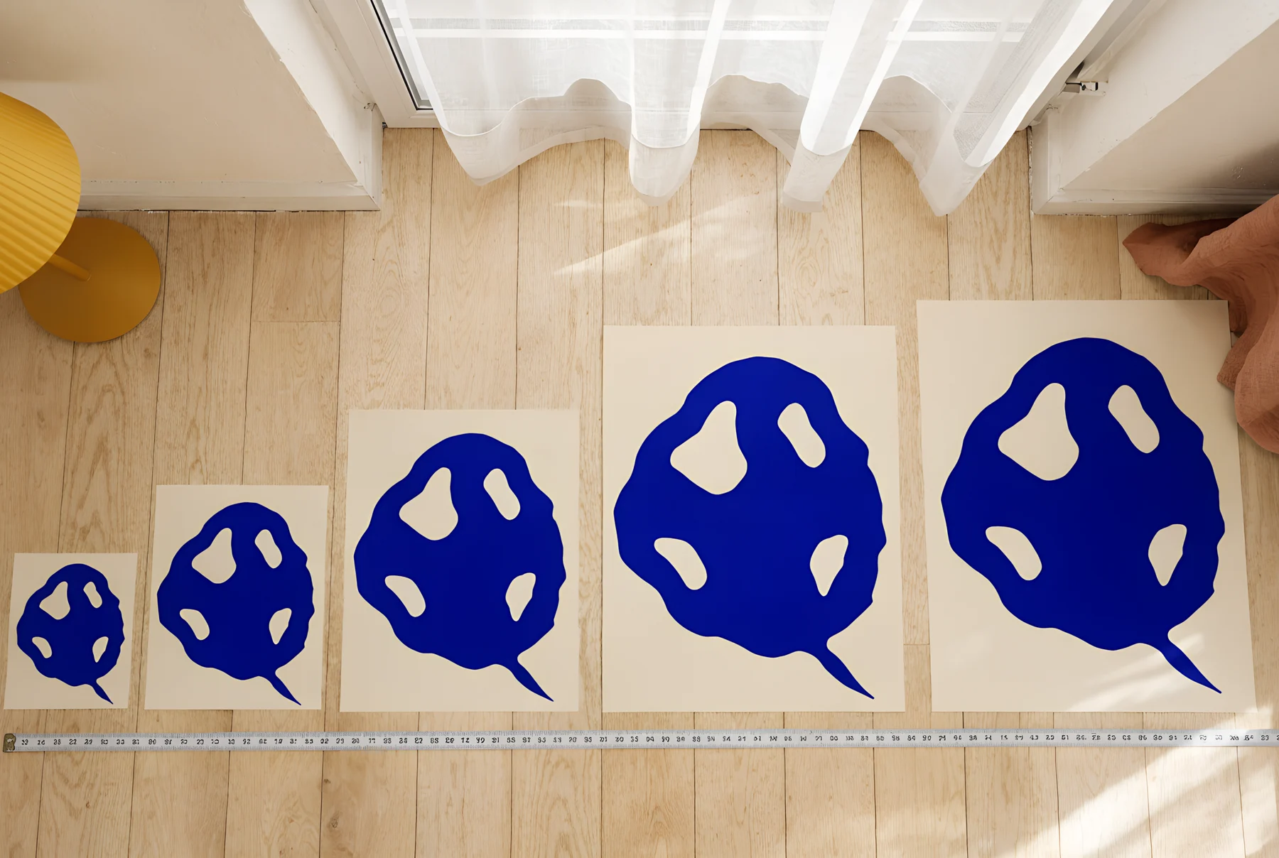 The same print at five sizes laid out on an oak floor beside a tape measure