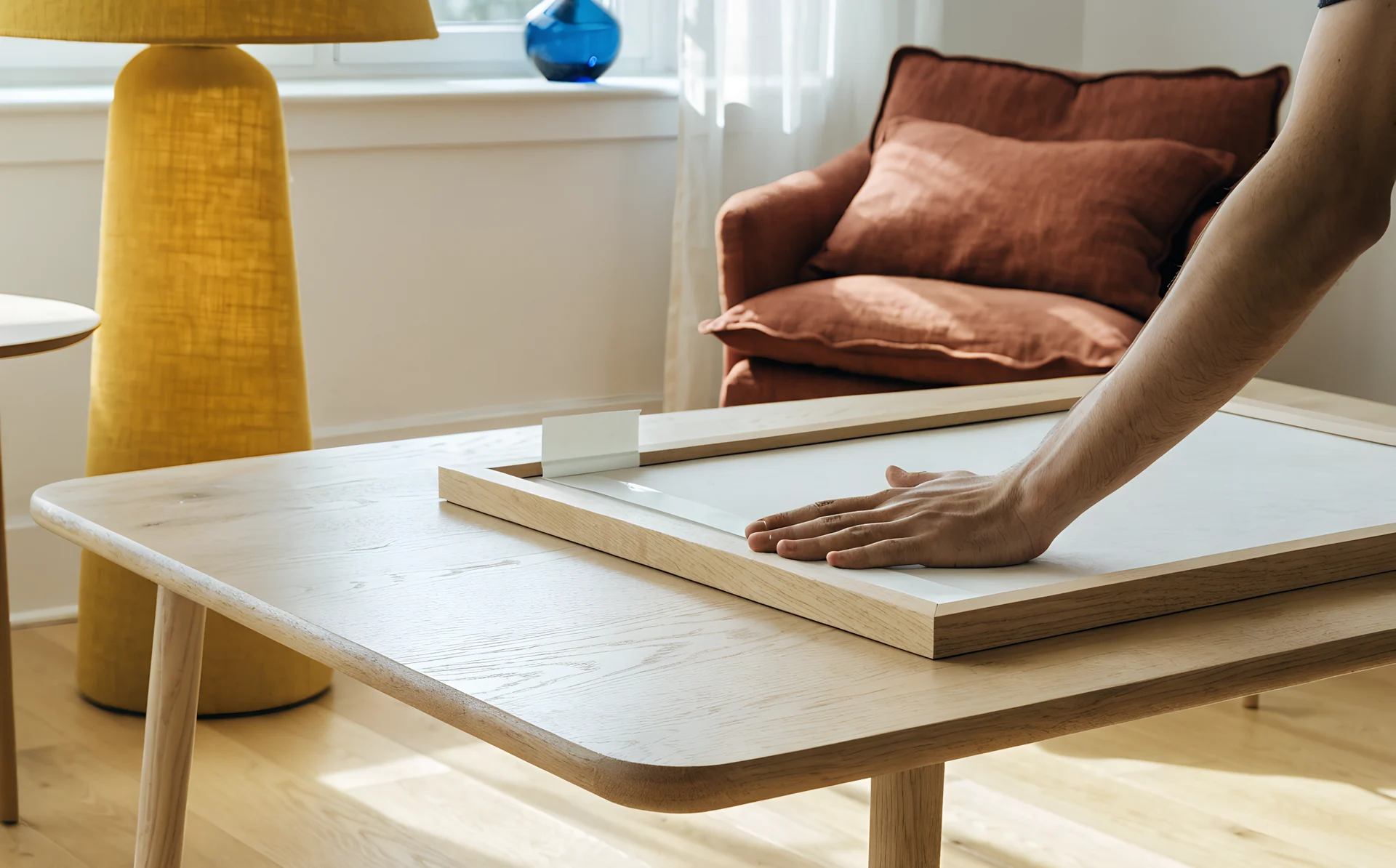A hand smooths an adhesive hanging strip onto the back of a light oak frame