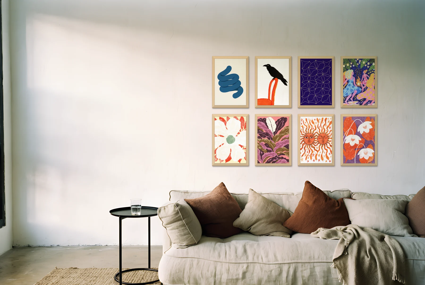 A gallery wall of eight light oak frames with bold, colourful prints above a linen sofa