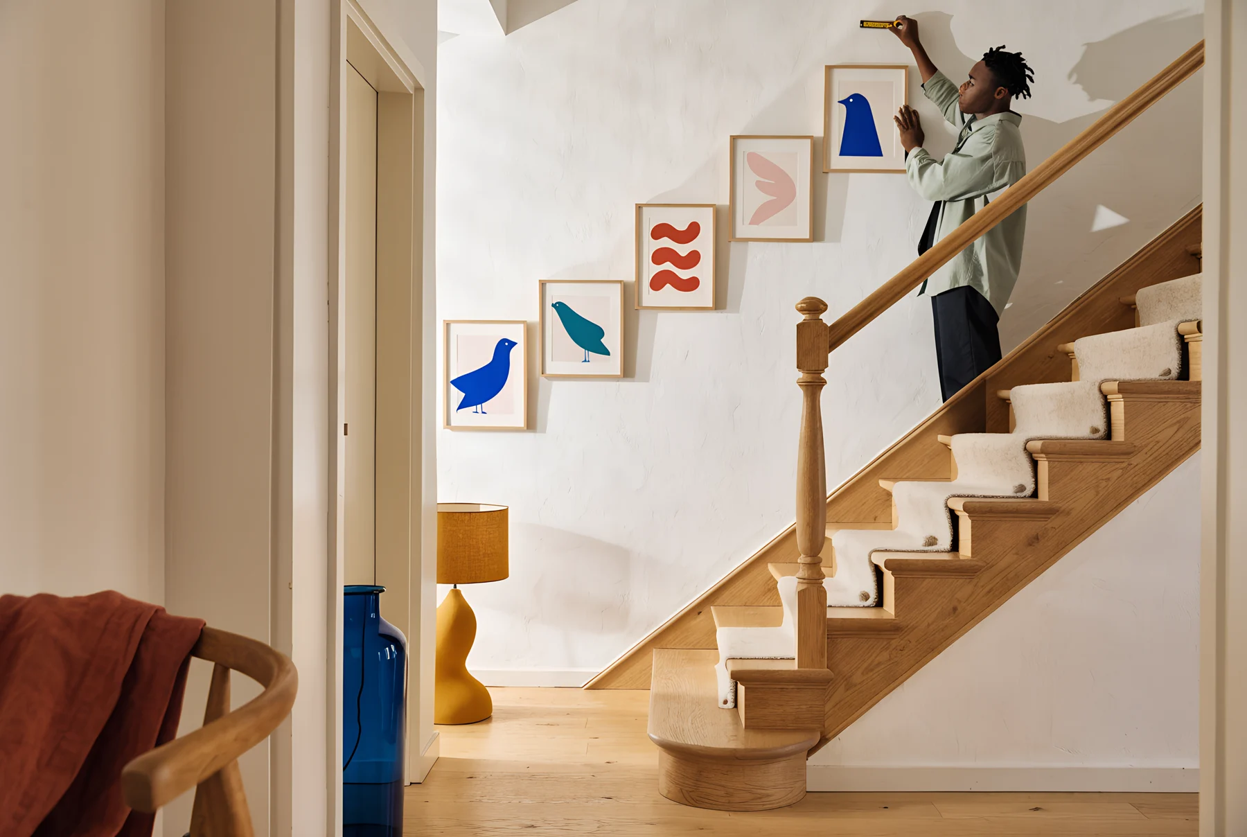 A man on the stairs measures the wall before hanging a staircase gallery