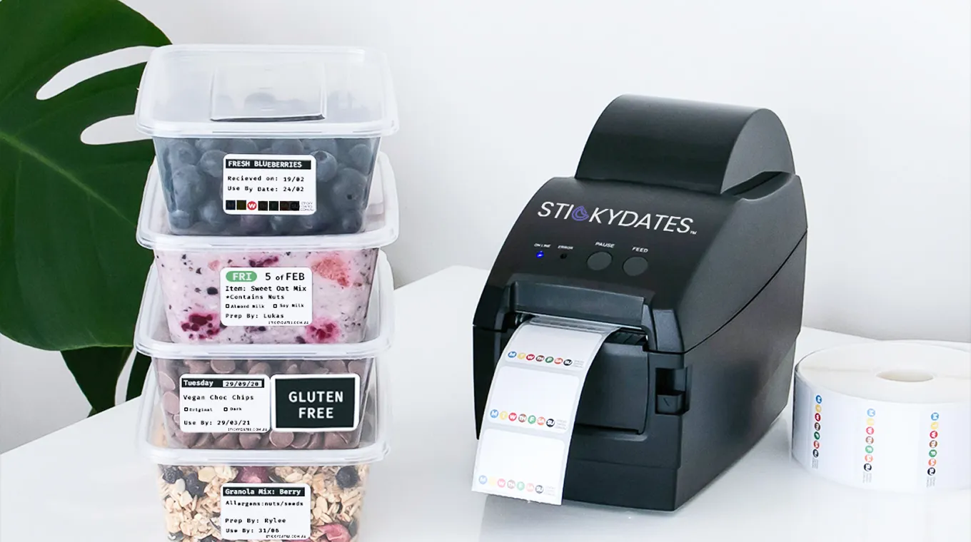 Black label printer next to stacked food containers with detailed allergy and date labels.