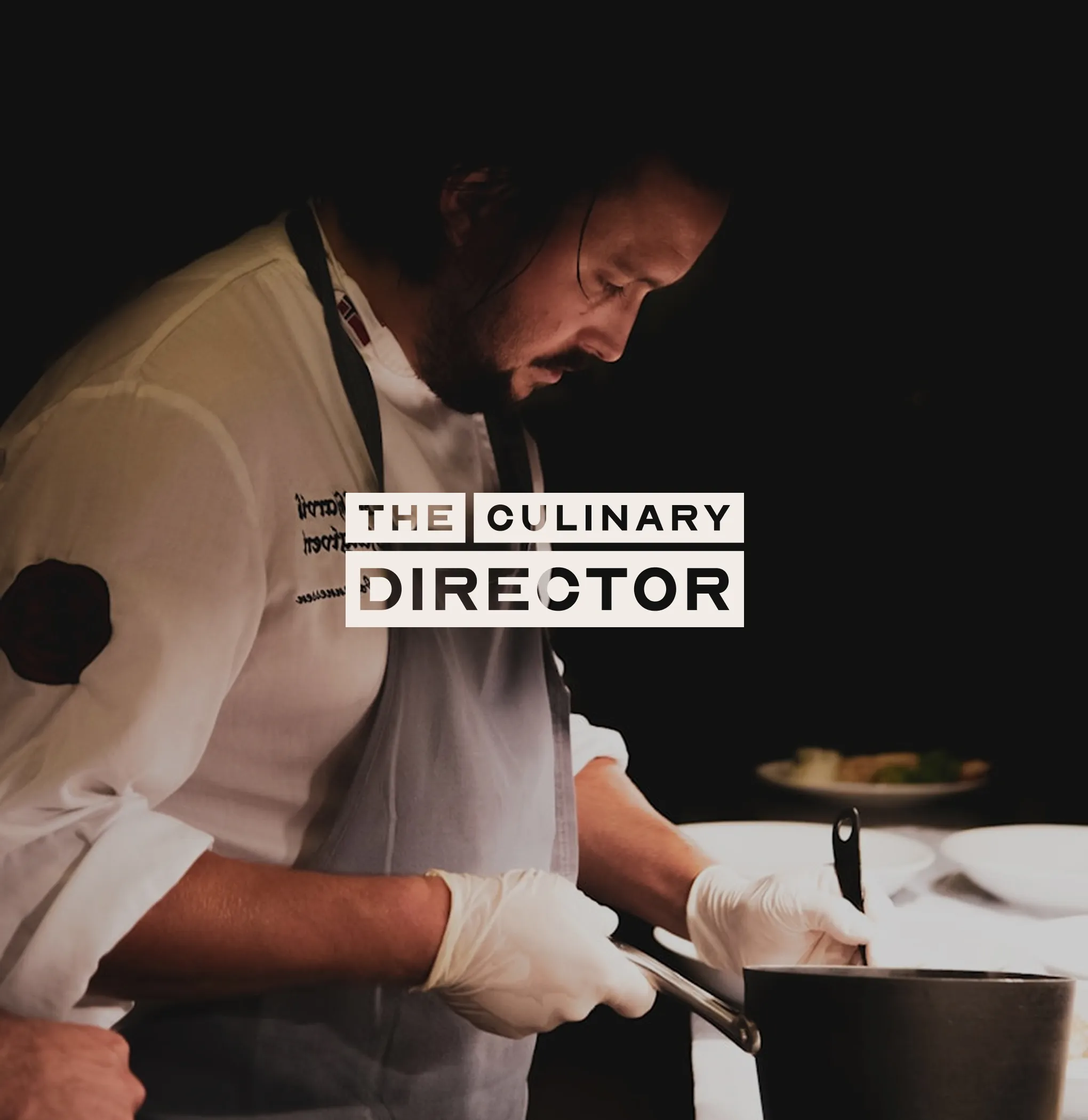 Chef wearing gloves and apron focused on cooking in a pot in a dimly lit kitchen.