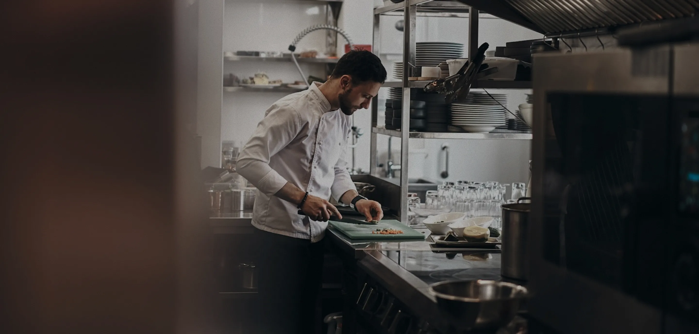 Chef in a white coat chopping food on a cutting board in a professional kitchen.