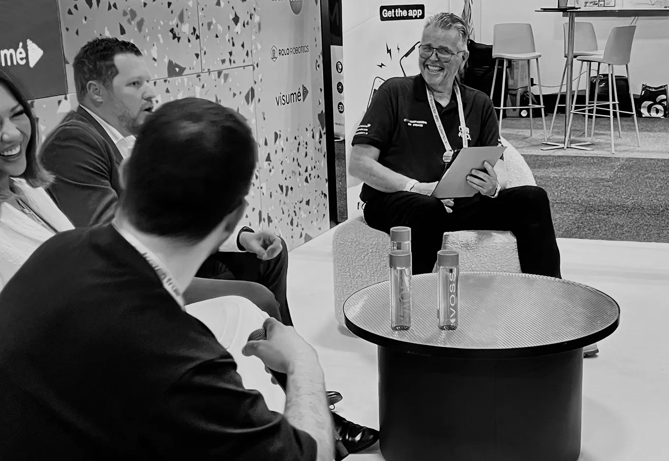 Four people sitting and chatting around a round table with two VOSS water bottles.