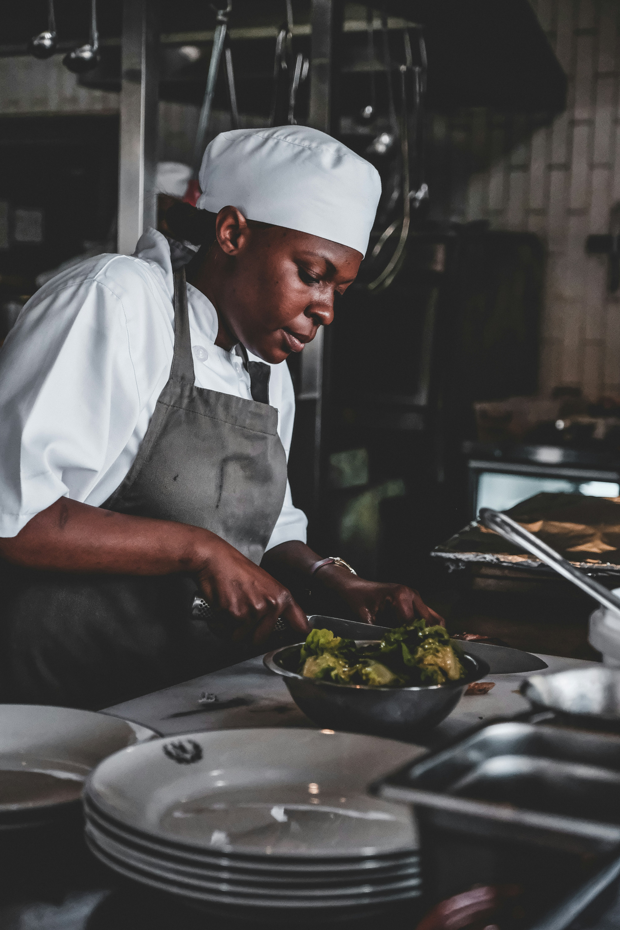 Chef in white hat and apron preparing food with lettuce in a bowl in a restaurant kitchen.