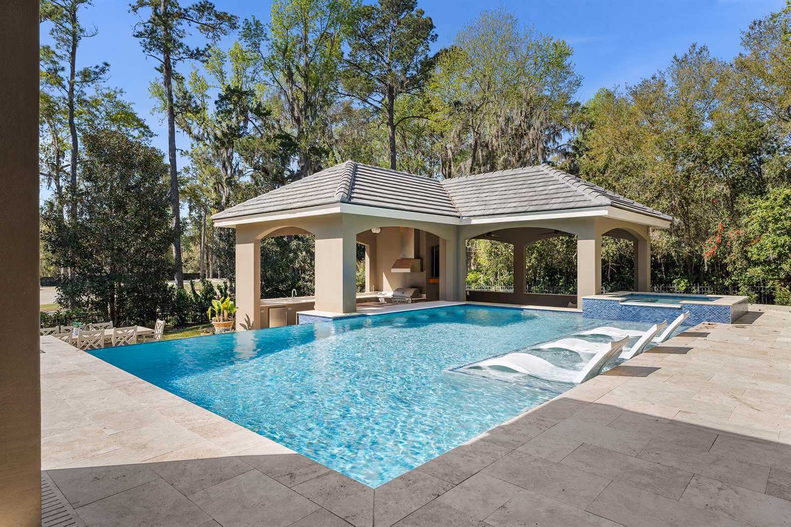 Pool with a tanning ledge and lounge chairs beside a poolside cabana