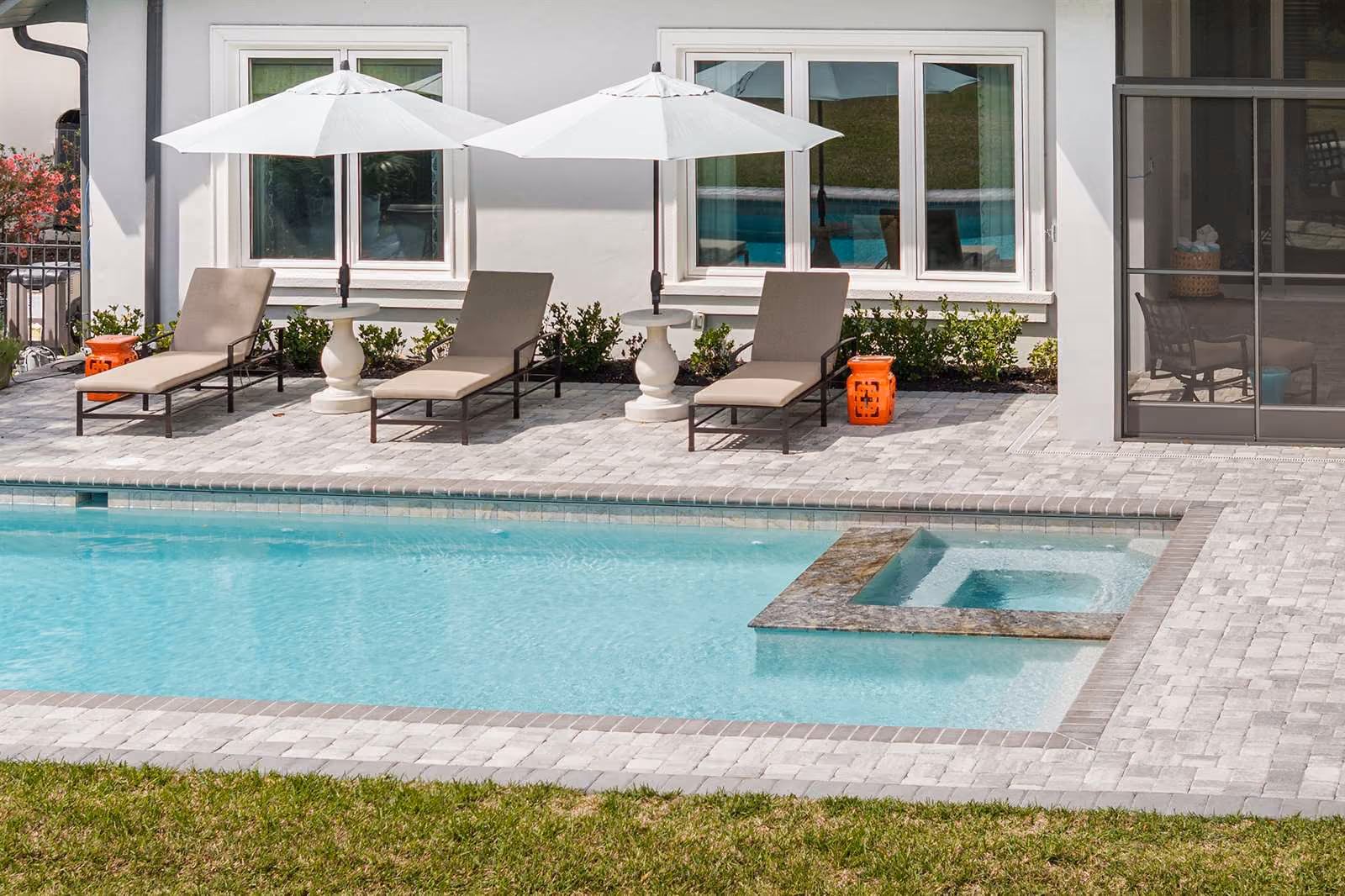 Pool with a raised stone spa, lounge chairs, and white umbrellas