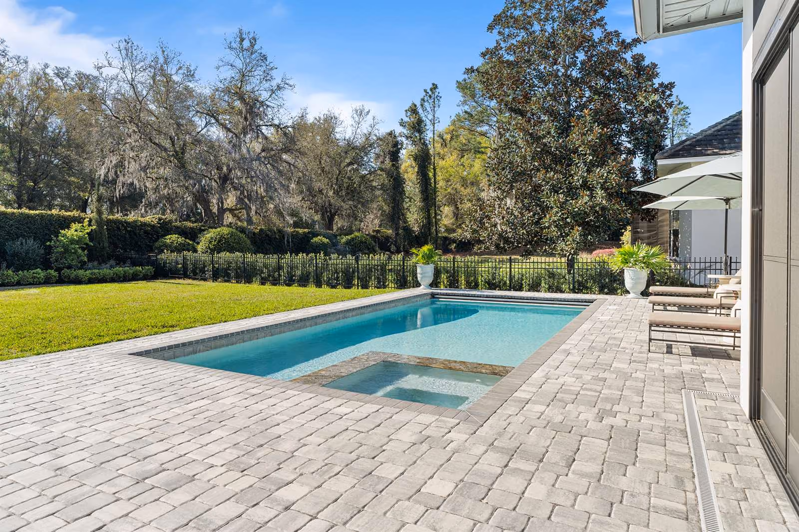 Geometric pool and spa on a paver patio in a fenced backyard