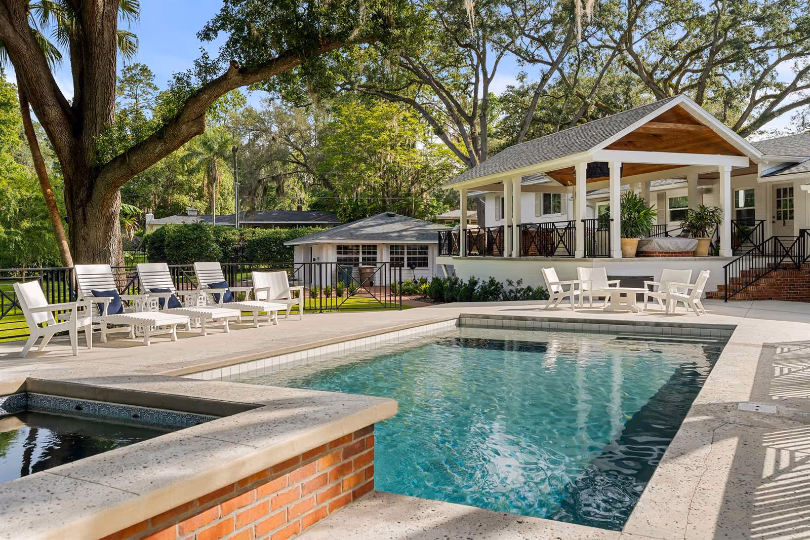 Backyard pool beside a covered patio shaded by oak trees