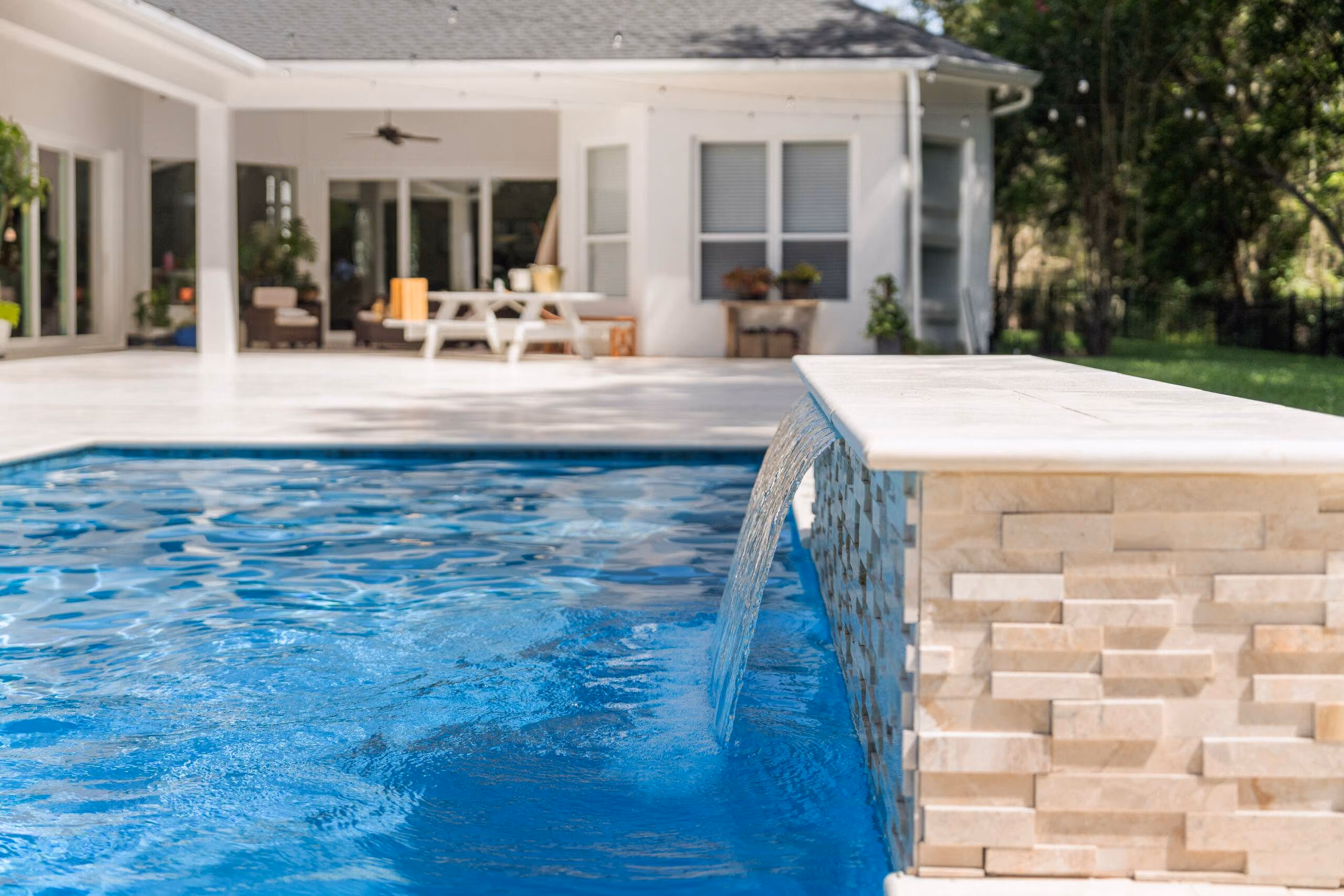 Backyard swimming pool with clear blue water and patio seating, managed by a smart pool automation system.