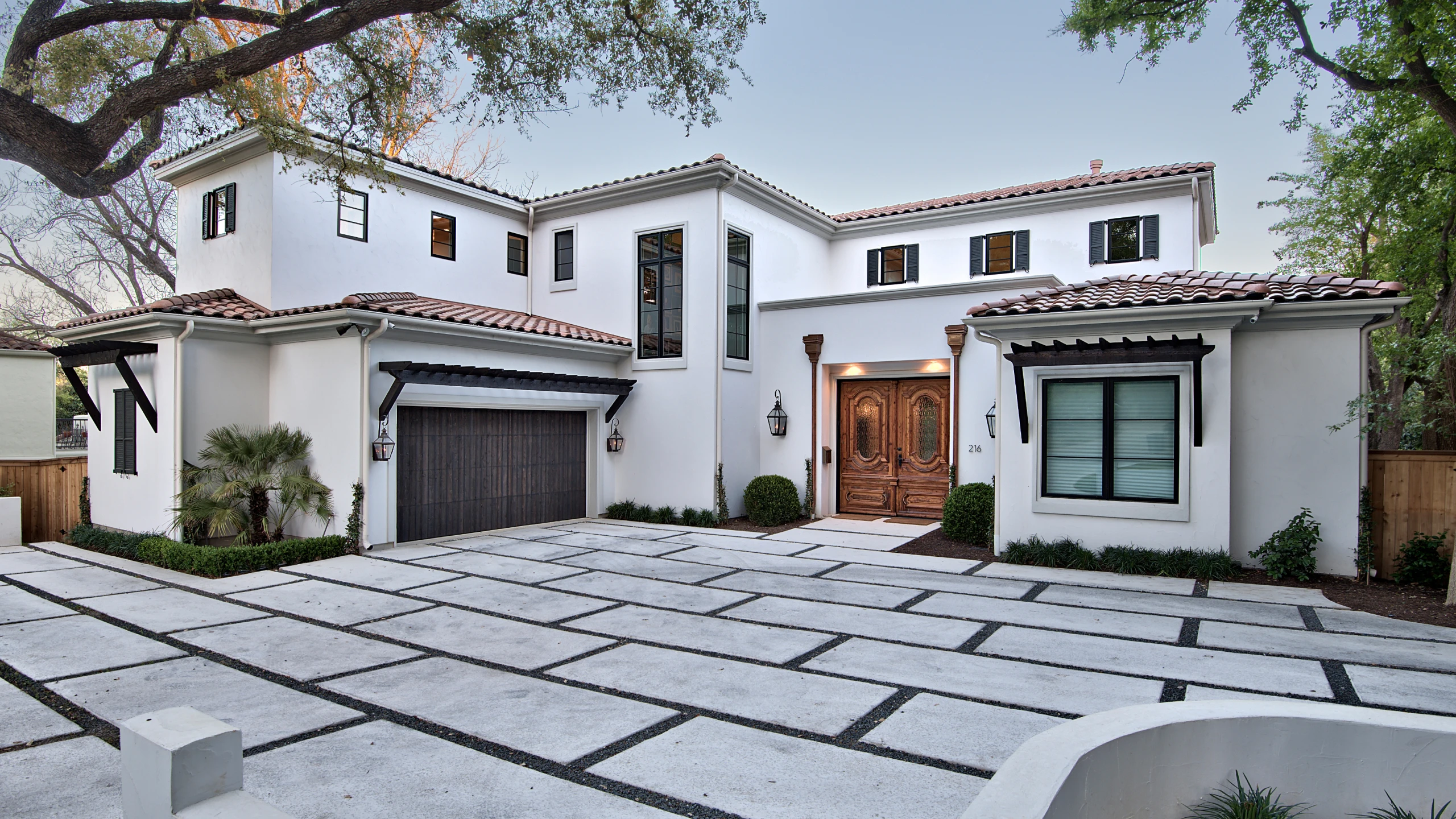White Mediterranean-style custom home with clay tile roof, carved wood entry doors and a paver driveway