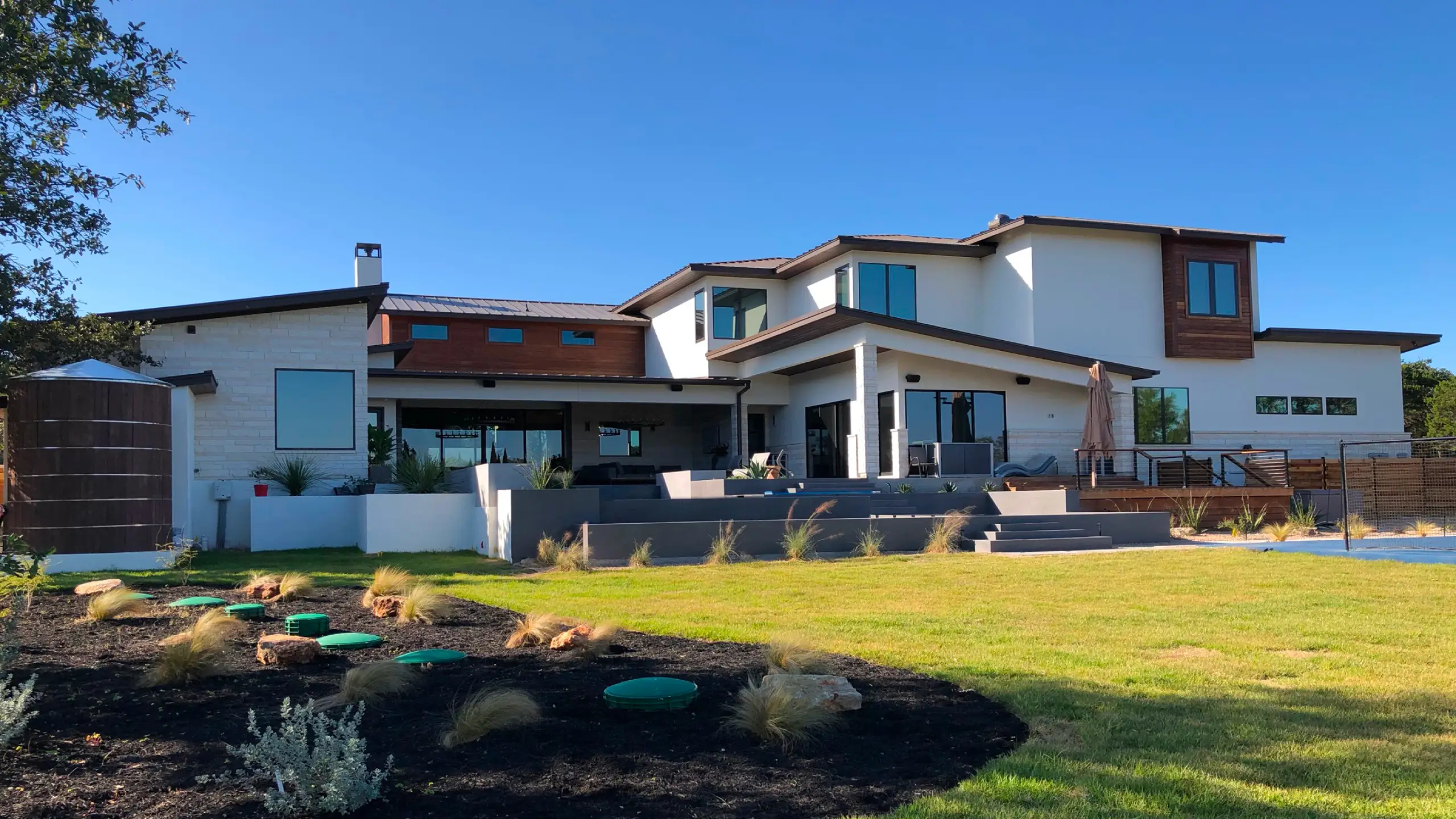 Modern Double Diamond custom home with white siding and cedar accents above a wide lawn and terraced stone patio